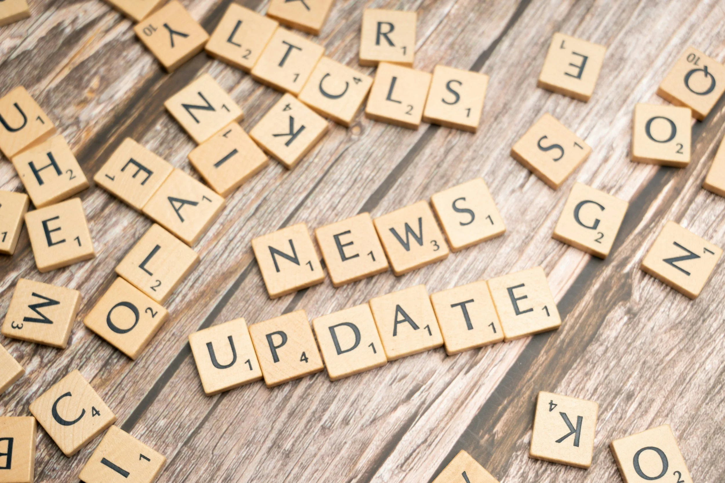 Scrabble tiles spelling out the words 'NEWS' and 'UPDATE' on a wooden surface.