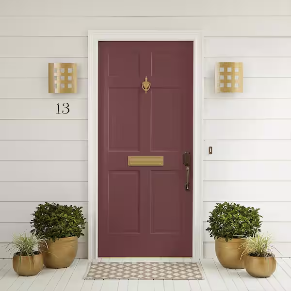 Front door of a house painted dark red with a brass knocker, mail slot, and handle. White siding with two wall-mounted light fixtures on either side of the door, house number 13, and potted plants at the entrance.