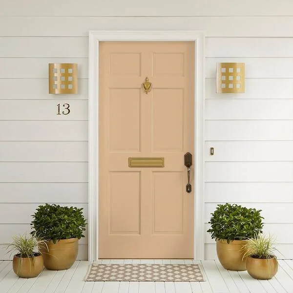 Front door of a house with white siding, beige door, gold hardware, and two wall-mounted lights. House number 13 displayed, with potted plants on each side of the door.