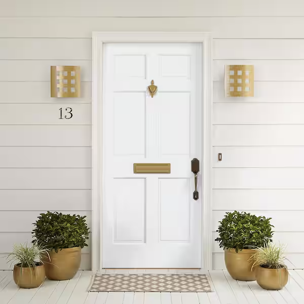 White front door with gold hardware, flank by two gold light fixtures, with house number 13 and potted plants on each side.