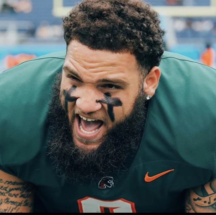 Close-up of a male football player with face paint, wearing a green jersey, shouting or celebrating on the field.