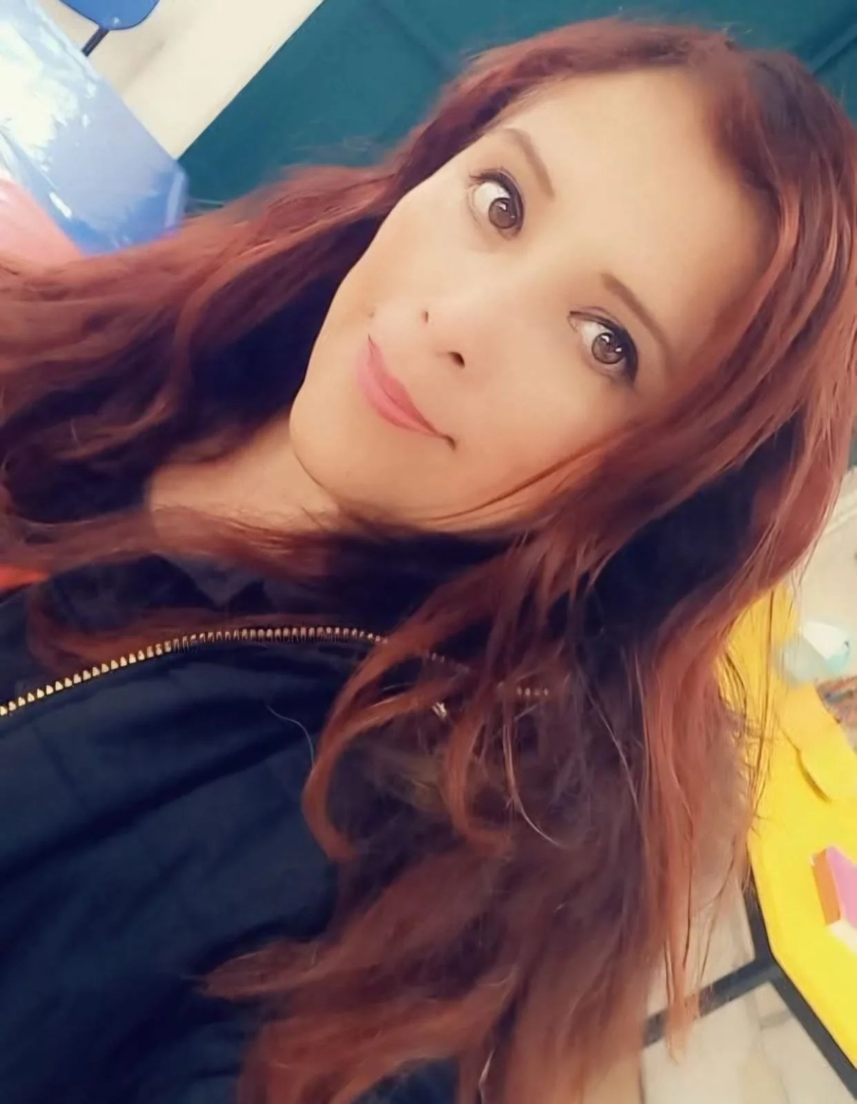Joven mujer con cabello rizado de color castaño rojizo sonriendo suavemente en un entorno interior.