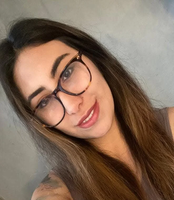 Joven mujer con gafas grandes de marco oscuro, cabello largo y liso, sonriendo y con fondo gris.