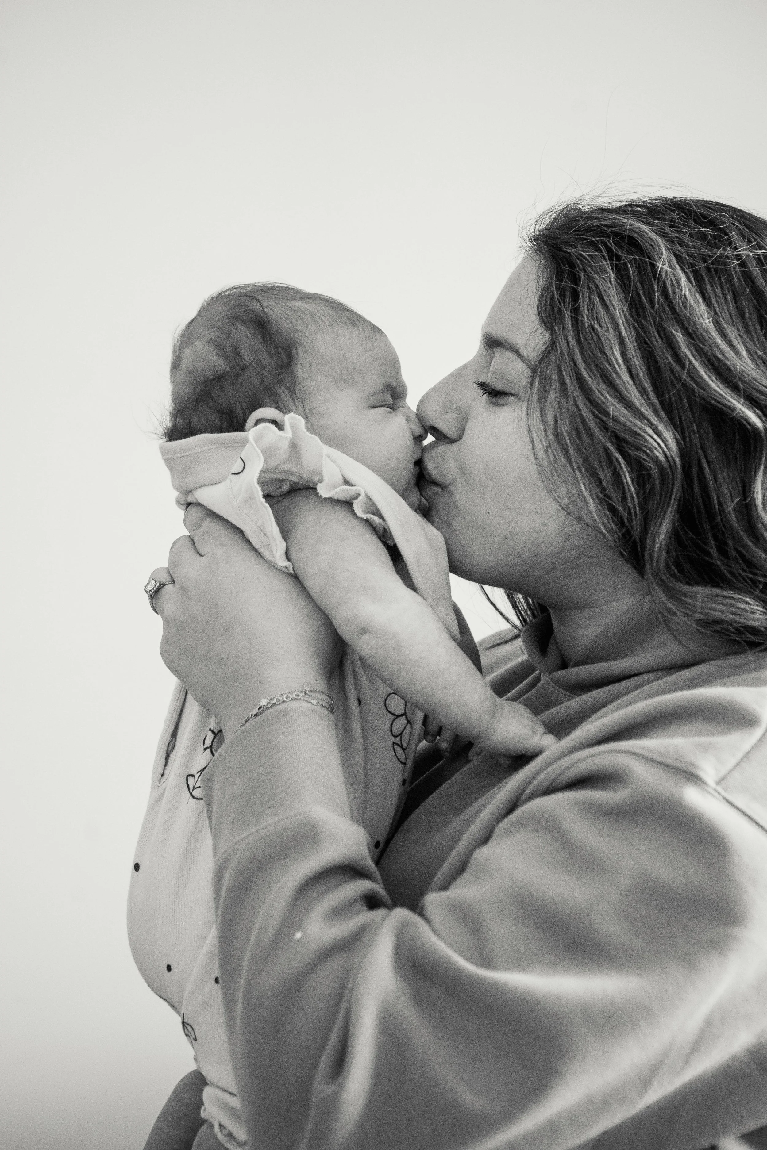 A woman holding a baby close, and they are touching noses in a kiss.
