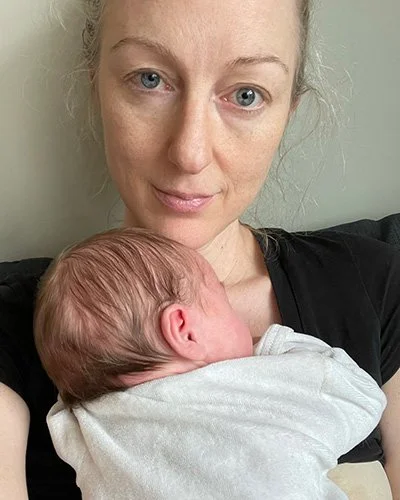 A woman holding a sleeping baby close to her chest, both are indoors.