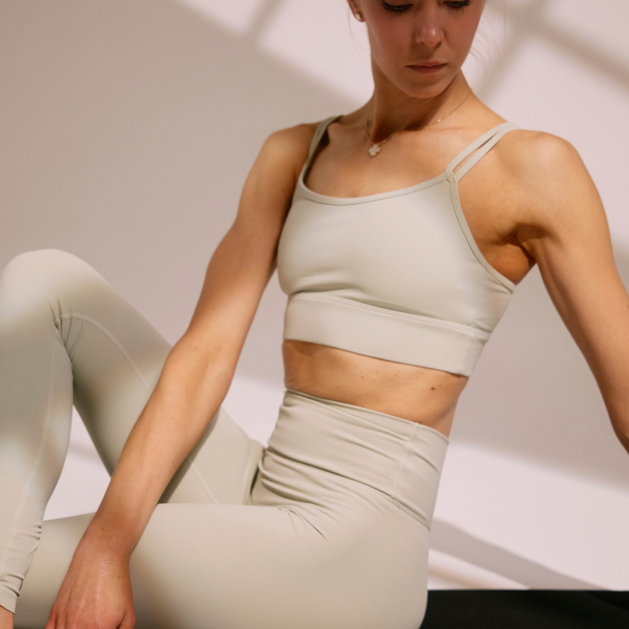 A woman in a beige sports bra and matching leggings sitting on the floor indoors.