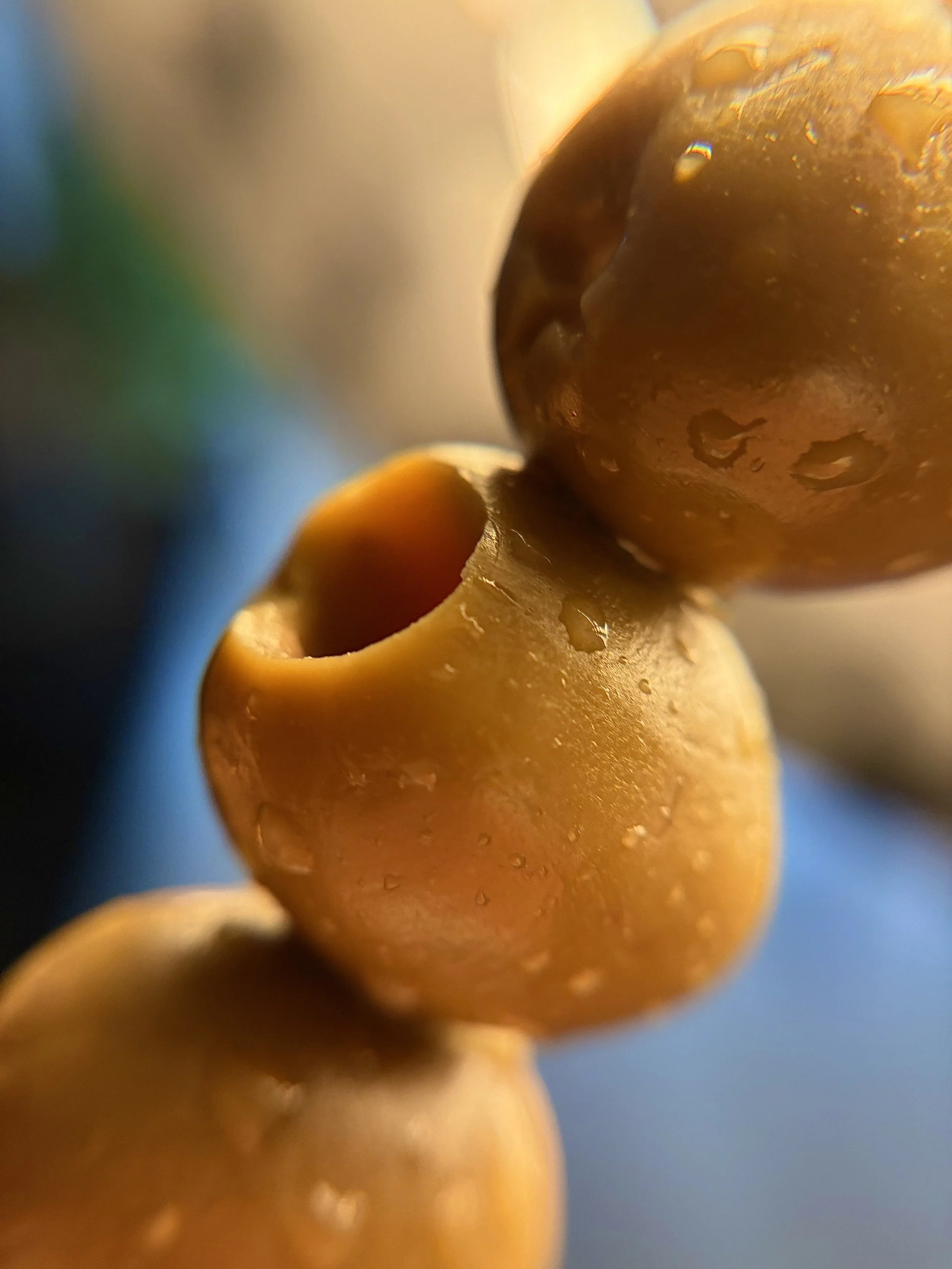 Close-up of three rinsed yellow or green olives with water droplets on their surface, stacked together.