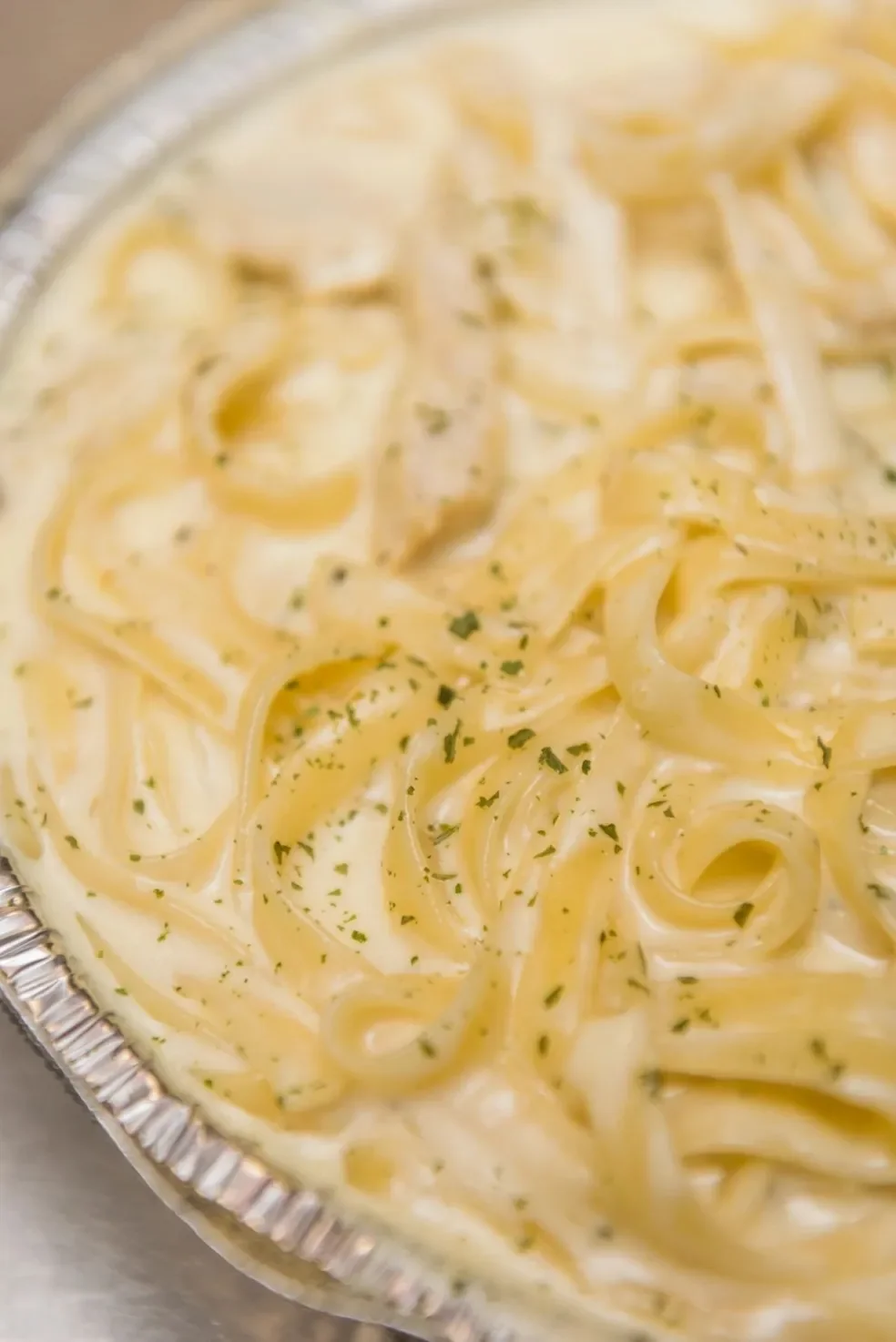 Close-up of creamy pasta with herbs in a foil container