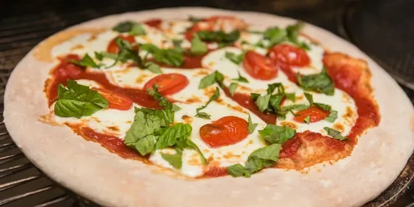 Fresh homemade Margherita pizza with cheese, cherry tomatoes, and basil leaves on a white crust.