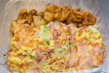A serving of potato salad with diced potatoes, ham, peas, and a creamy dressing