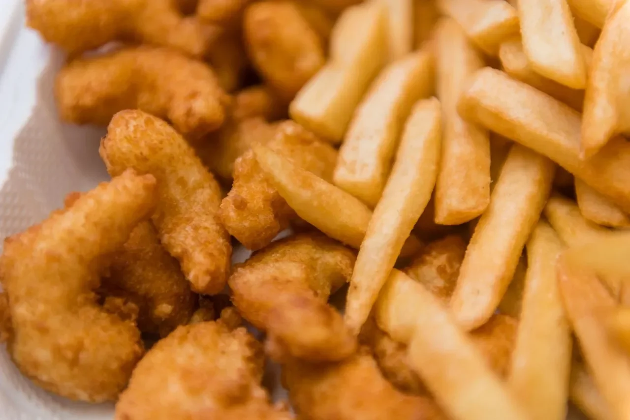 Close-up of fried chicken pieces and French fries on a white surface.