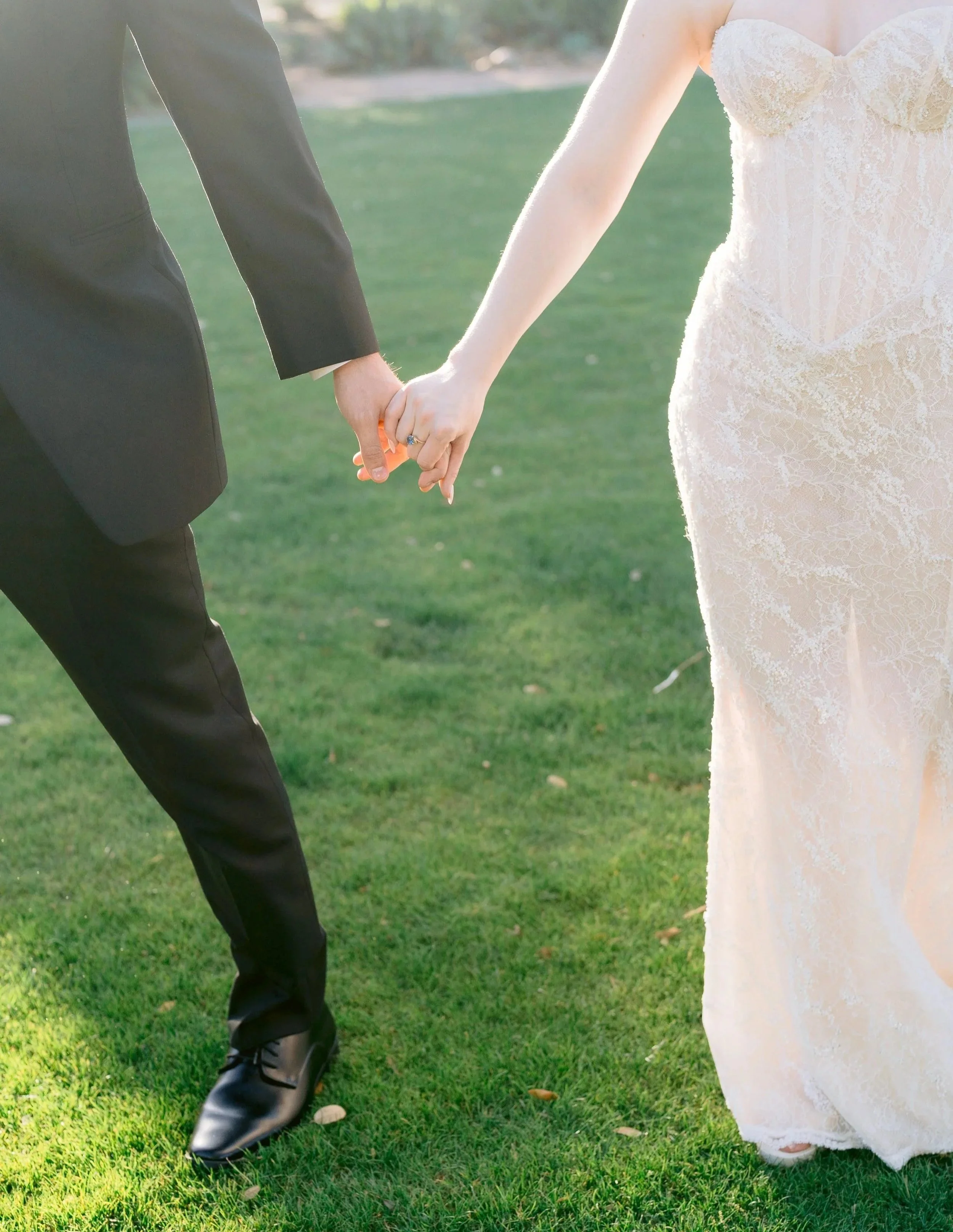 A bride and groom holding hands on a grassy outdoor area during their wedding.