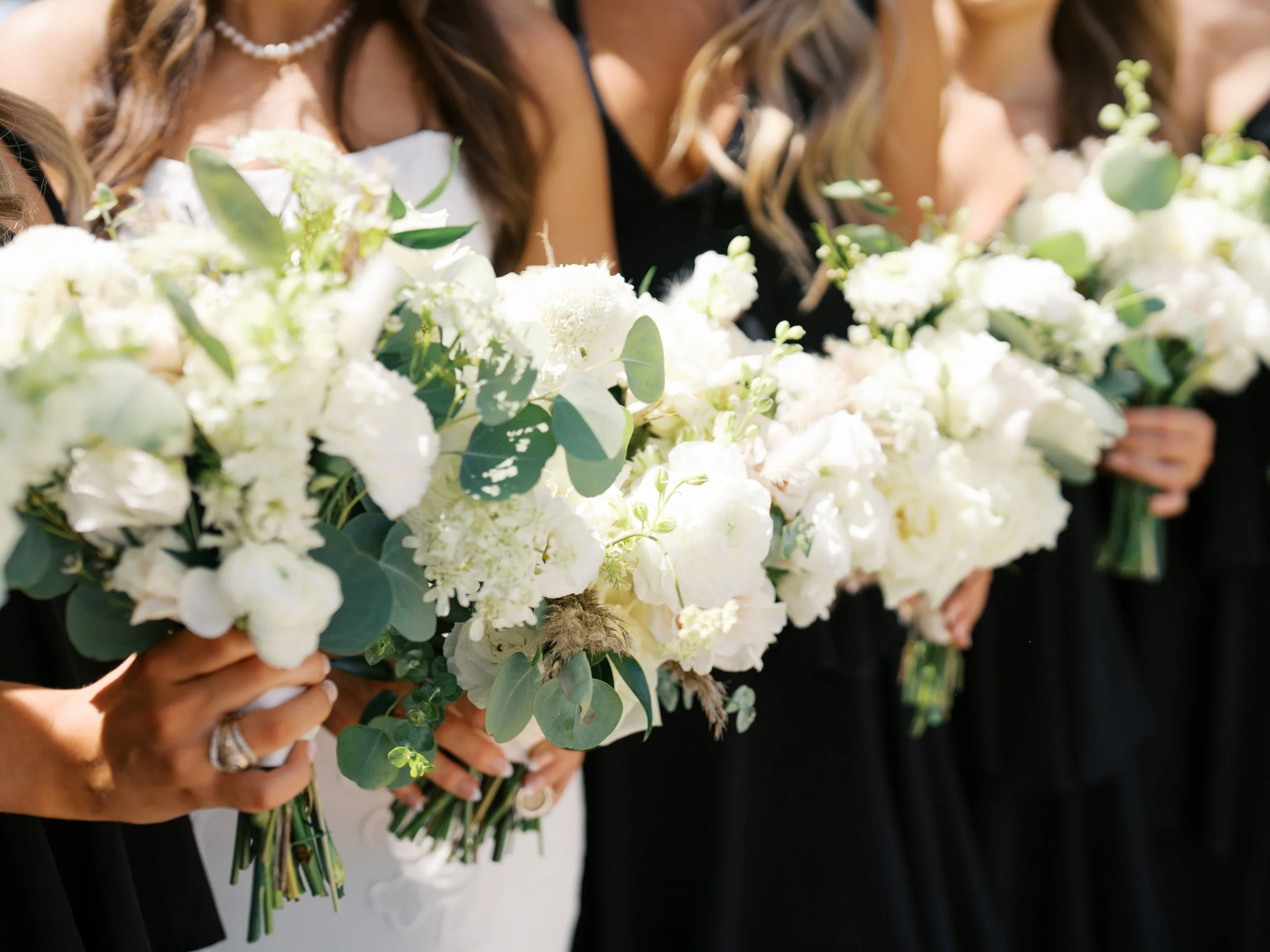 Bridesmaids and bride holding large bouquets of white flowers with eucalyptus leaves during a wedding.