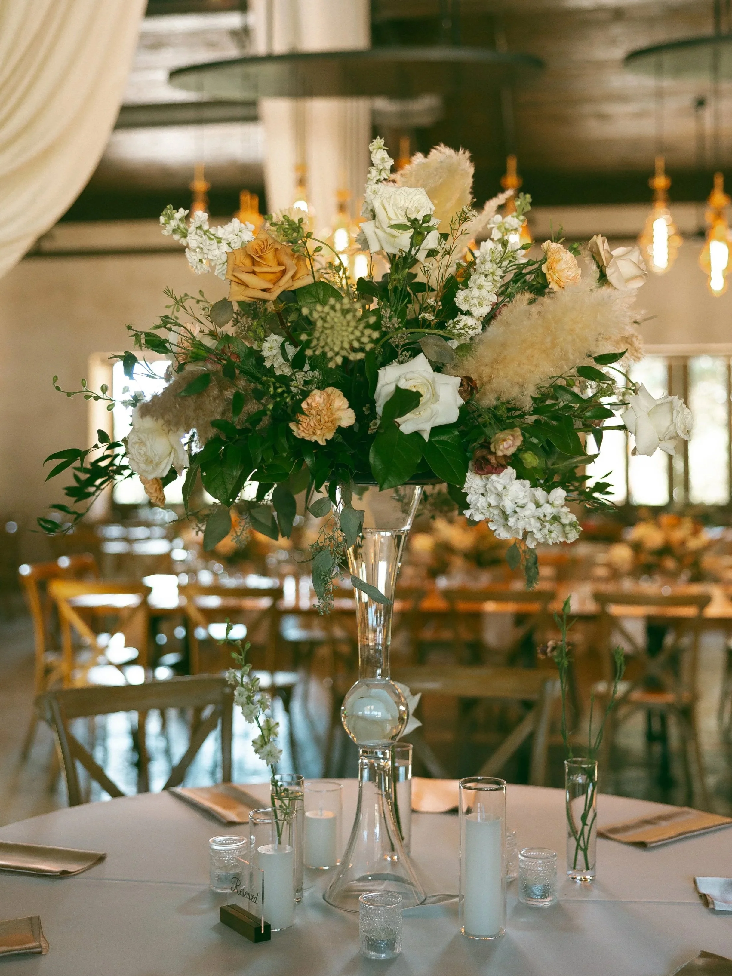 A tall floral centerpiece with white, peach, and cream-colored flowers on a dining table at an elegant event.