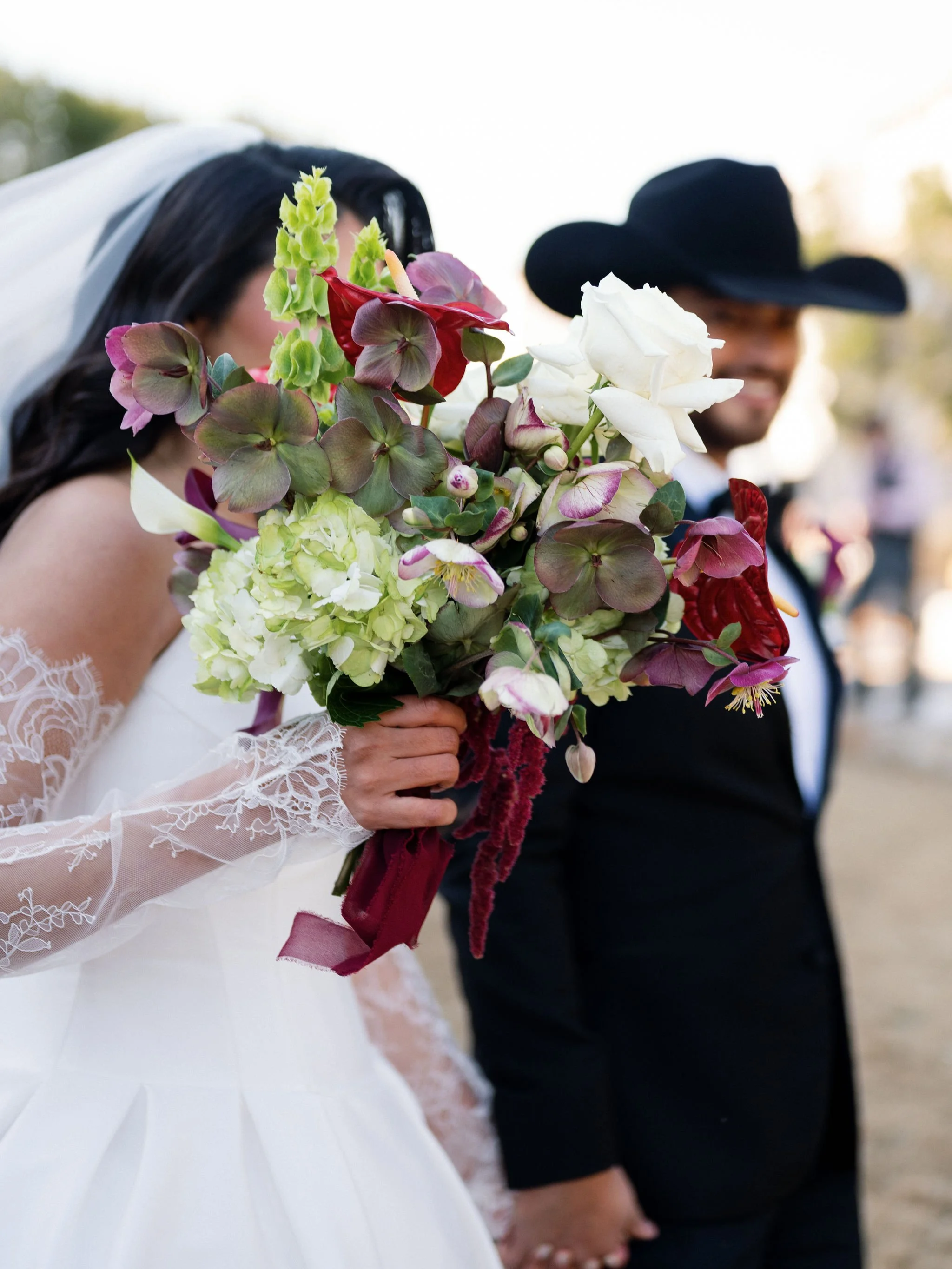 Bride and groom at wedding holding hands with the bride holding a bouquet of flowers in the foreground.