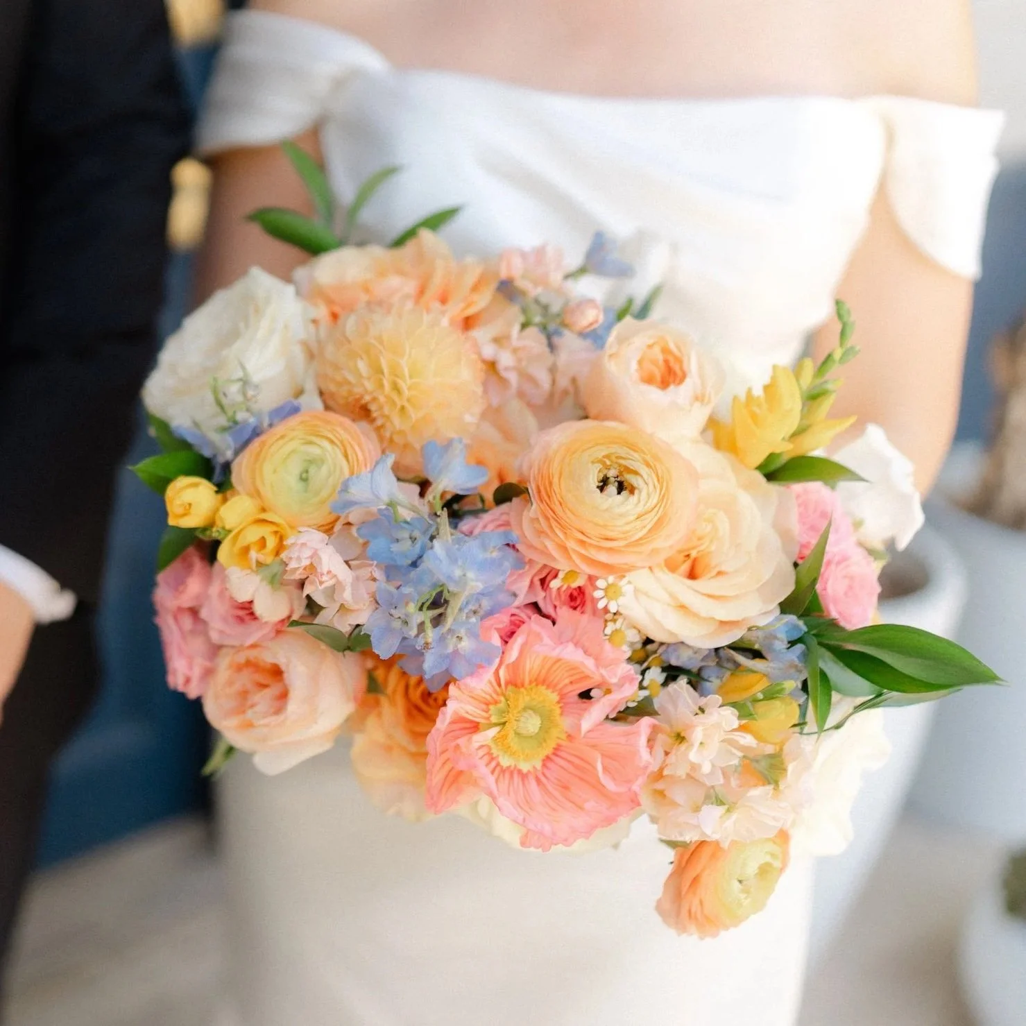 A person holding a bouquet of pastel-colored flowers, including peach, pink, yellow, and blue blossoms.