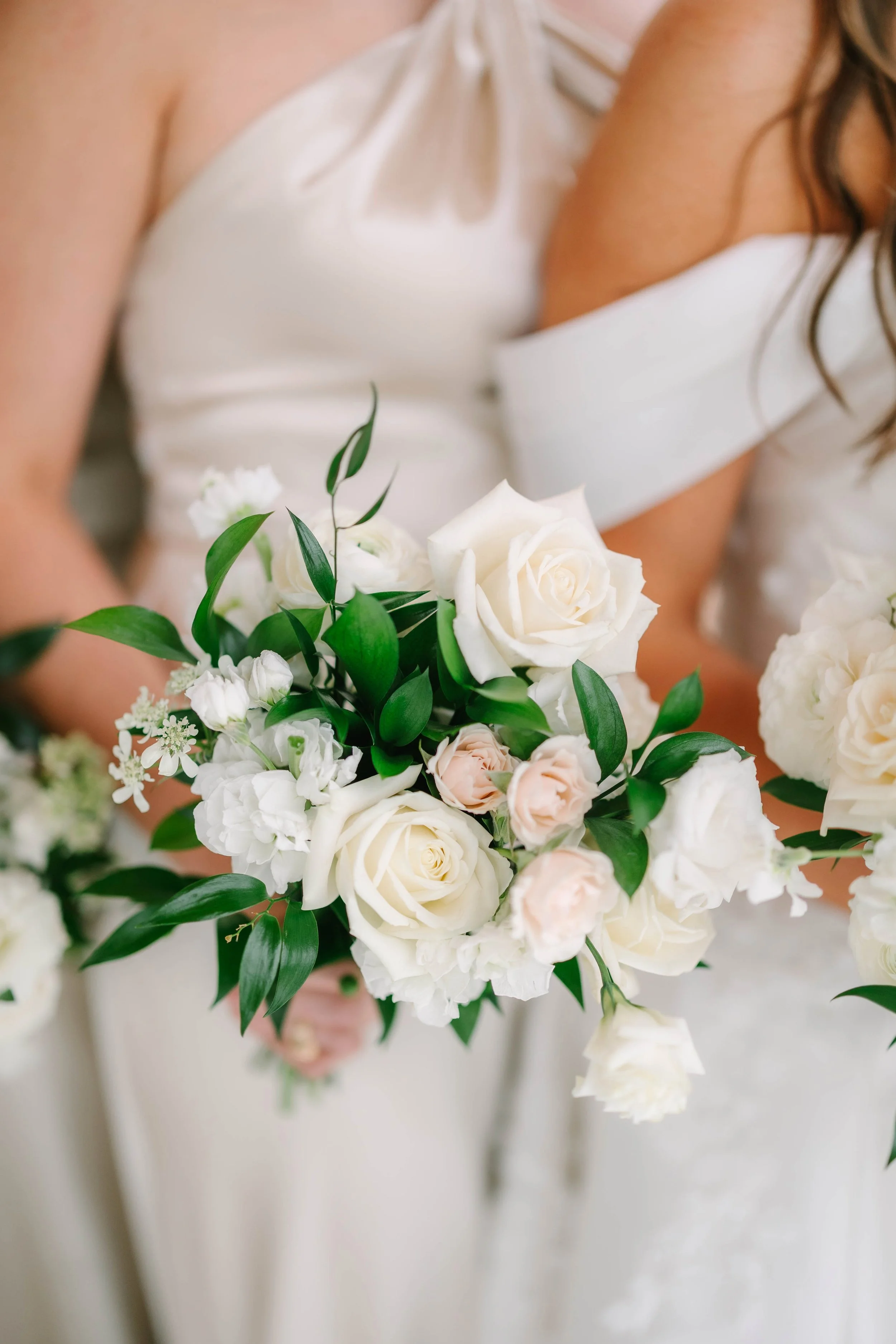 A bride holding a bouquet of white and pale pink roses with green leaves at a wedding.