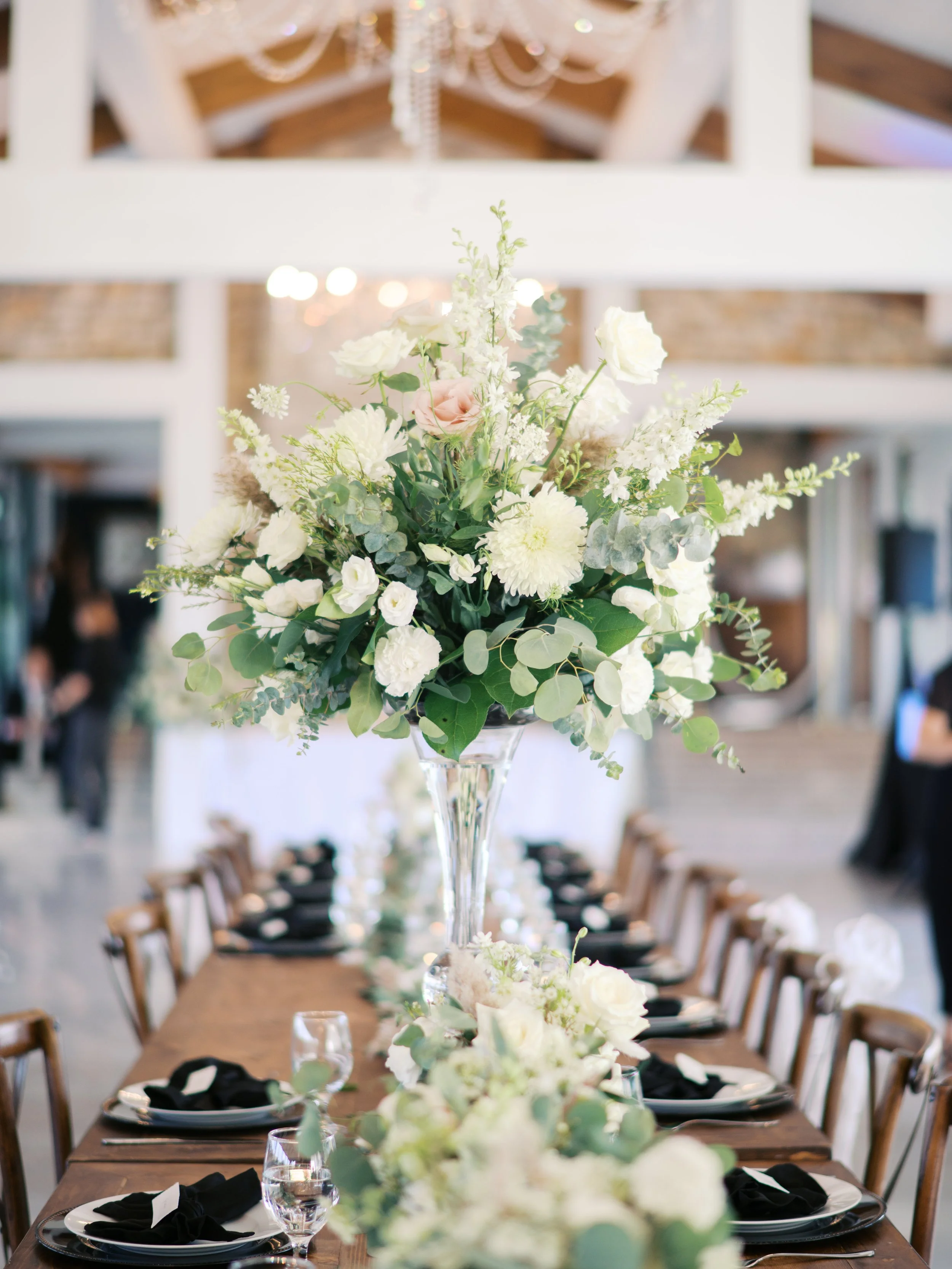 Elegant wedding table centerpiece with white and pale pink flowers, greenery, and candles on a decorated dining table.