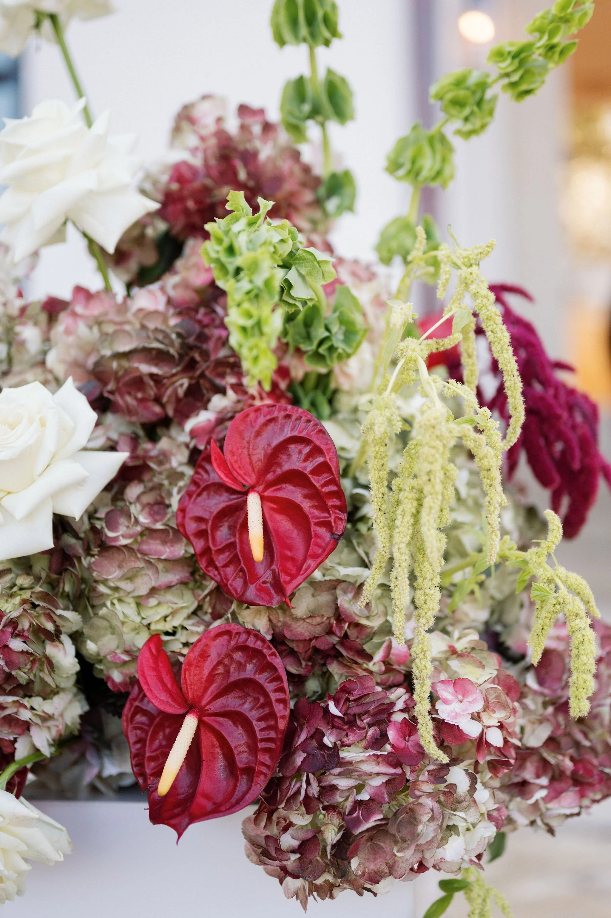 Close-up of a colorful flower arrangement featuring yellow, red, pink, green, and white flowers, including anthuriums, hydrangeas, and other floral varieties.