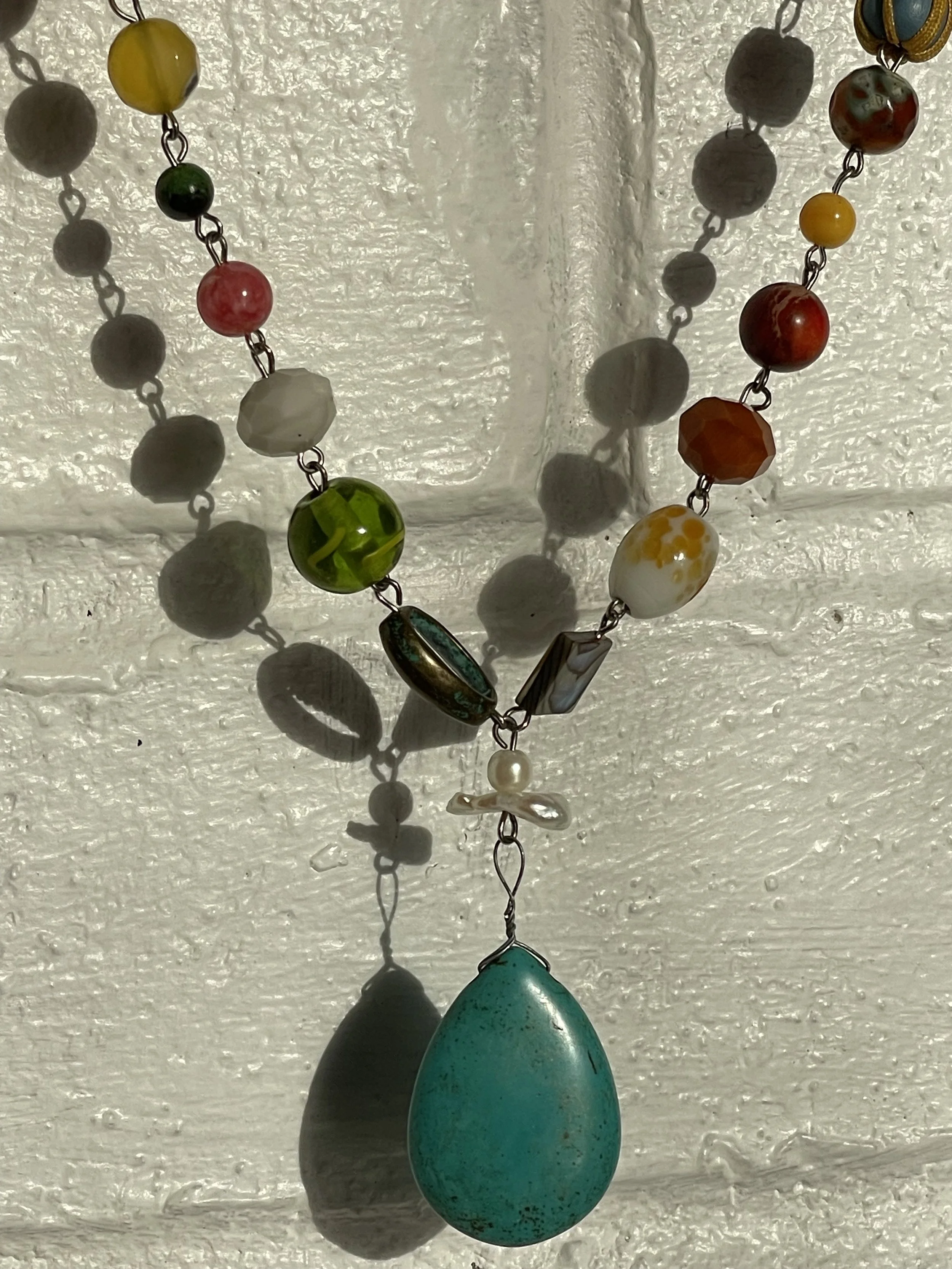 Close-up of a colorful beaded necklace hanging against a textured white wall, casting shadows.