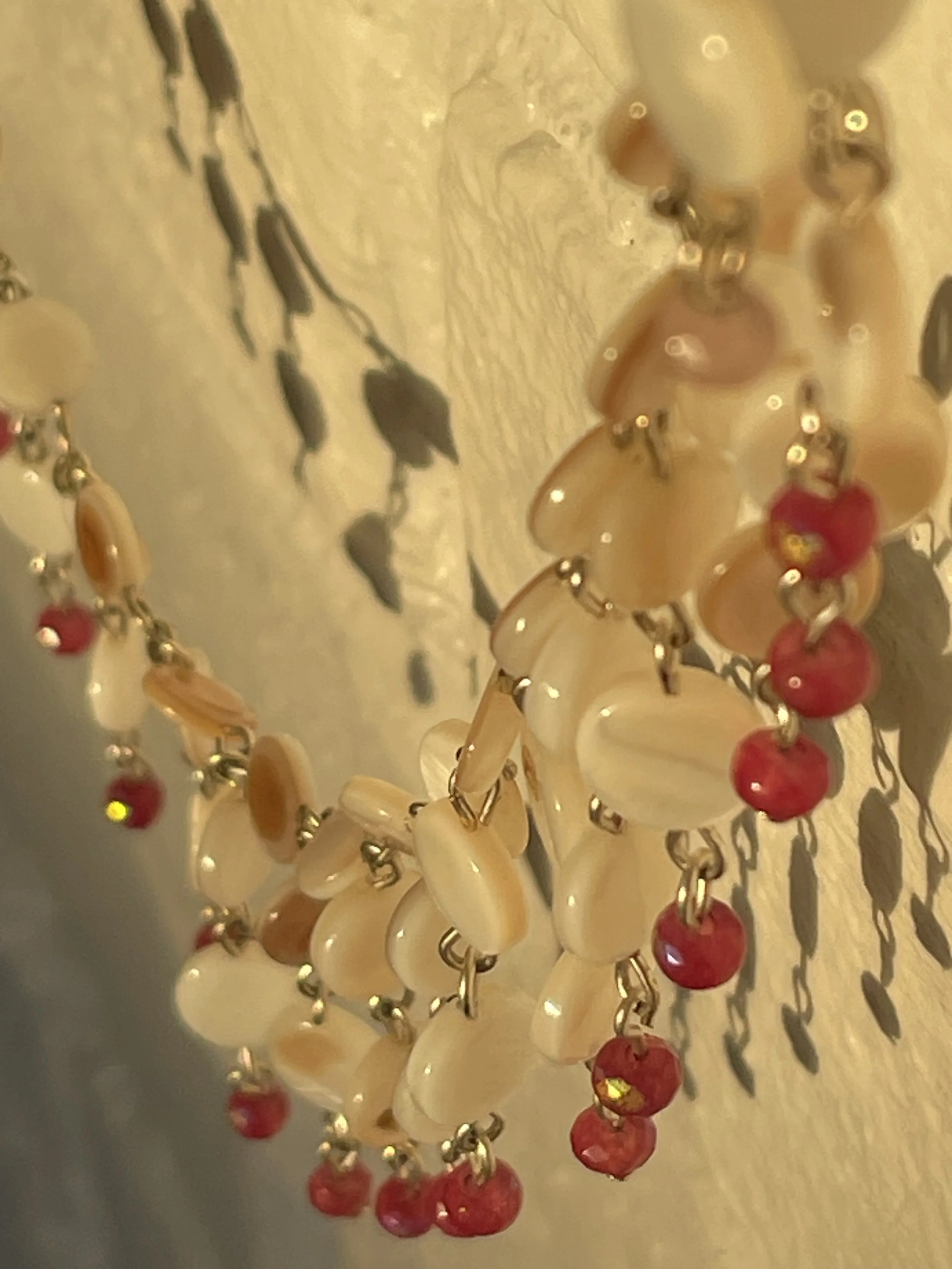 Close-up of a beaded necklace with cream, red, and metallic beads resting on a textured beige surface.
