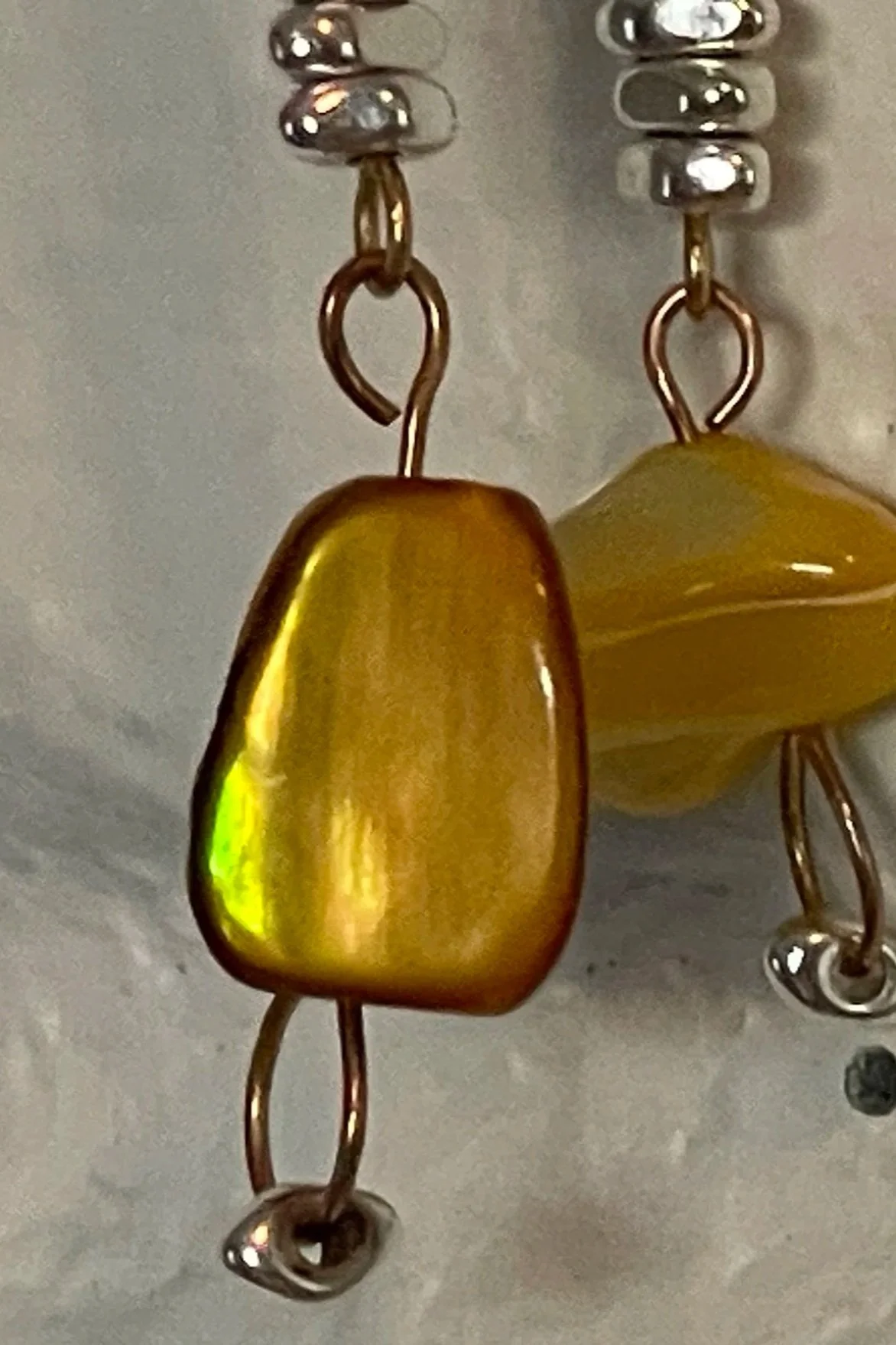 Close-up of a fishing jig with a shiny, gold-colored body and metal hooks, hanging against a neutral background.