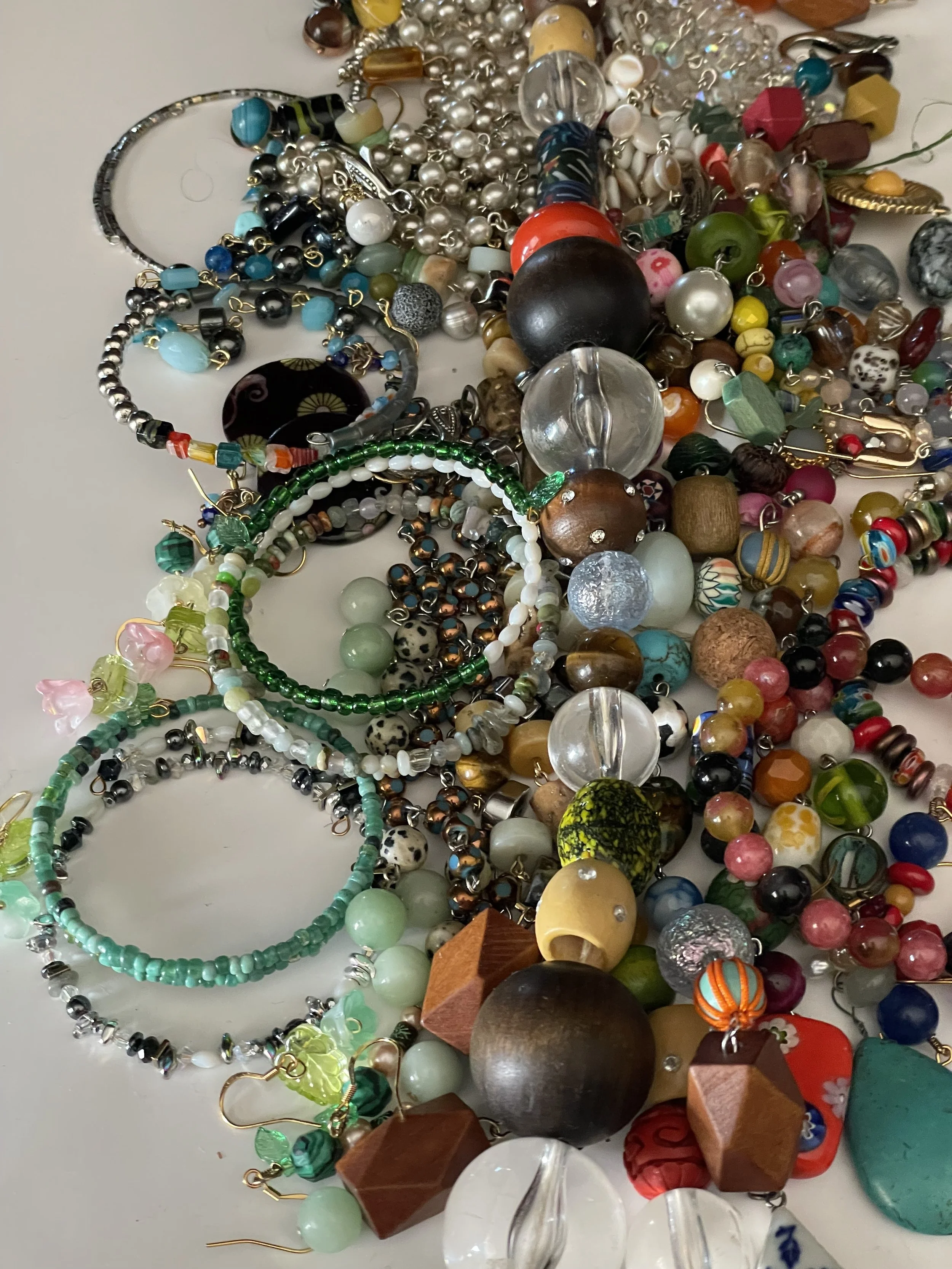 A pile of assorted jewelry including necklaces, bracelets, and beads with various colors, shapes, and materials including glass, plastic, and metal.