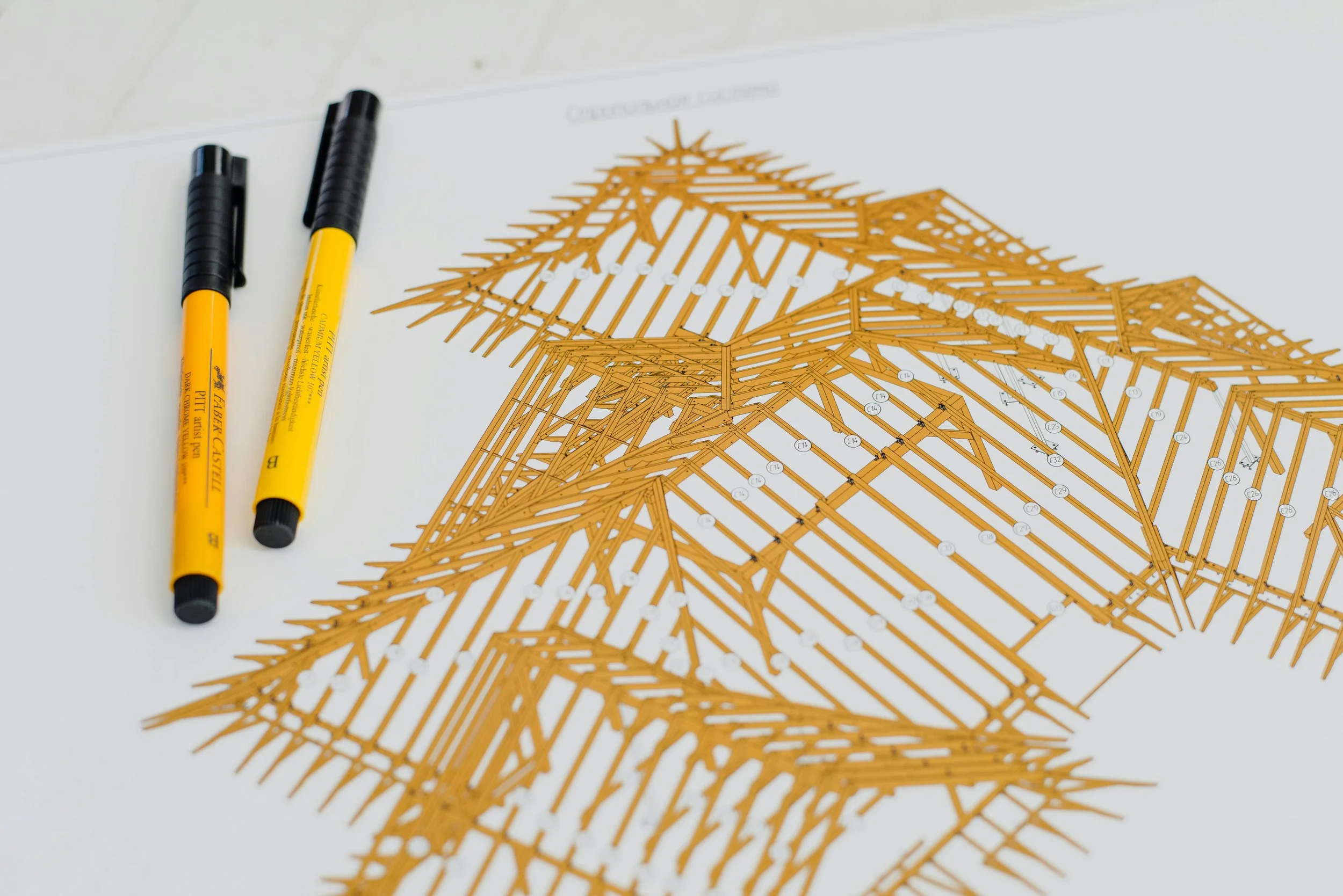 Architectural blueprint with orange wooden model parts, two yellow and black markers on white paper background.