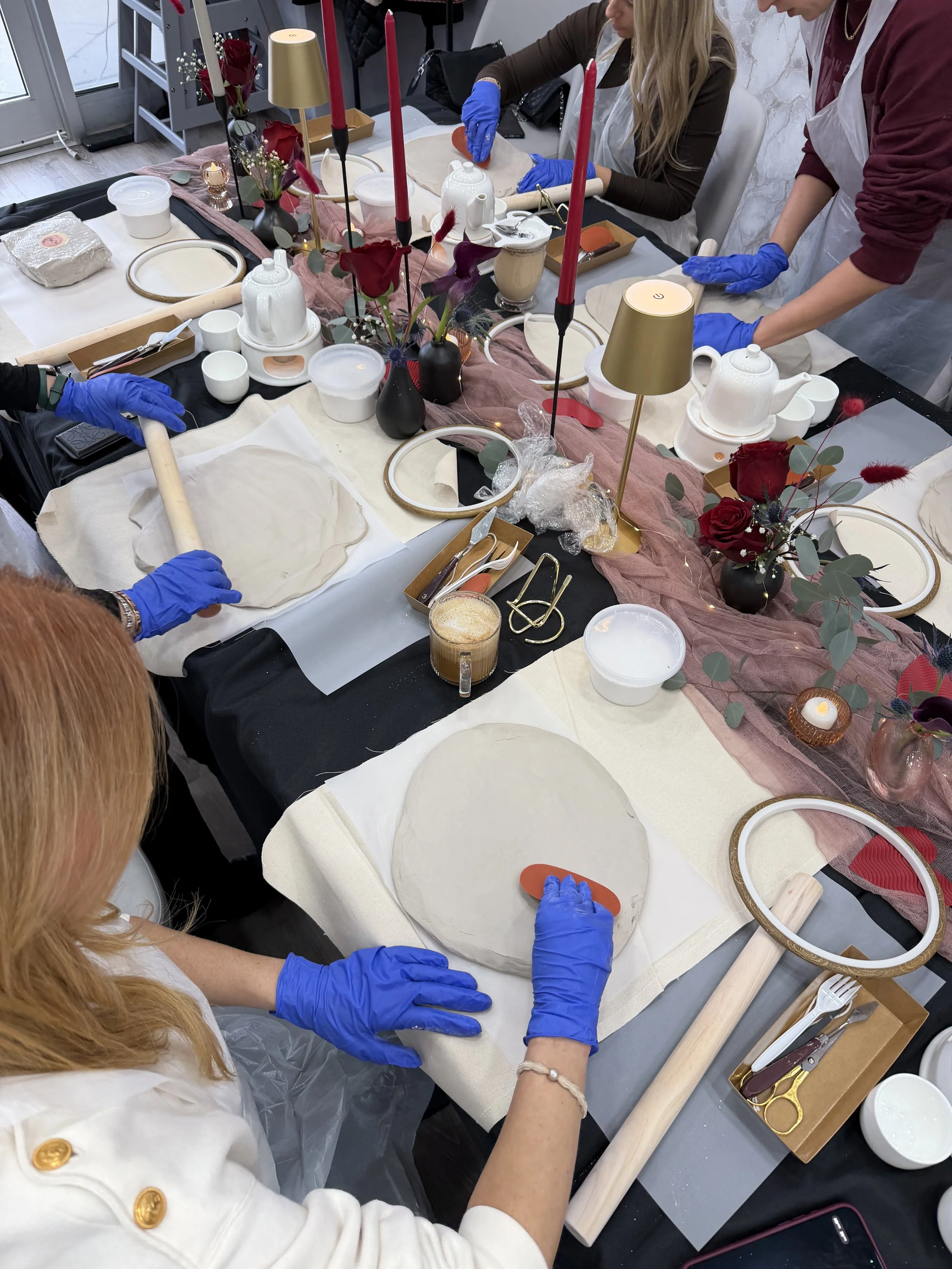 People wearing blue gloves decorating a table with floral arrangements, candles, and tableware for a craft or event.