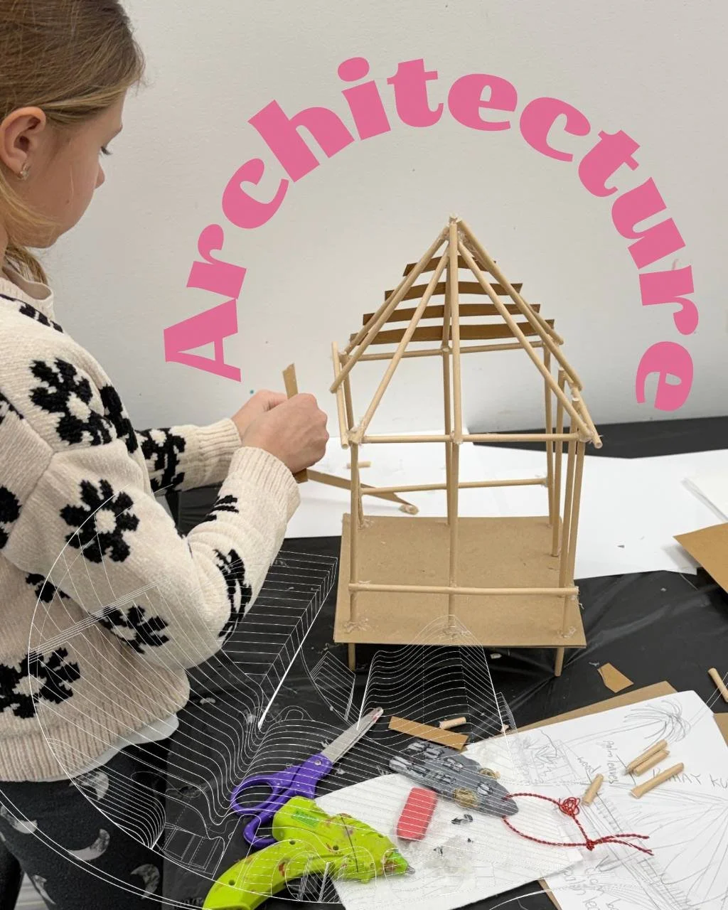 A girl working on a project with wooden sticks and paper, sitting at a table with crafting tools and sketches, in front of a wall with pink letters spelling "Architecture".