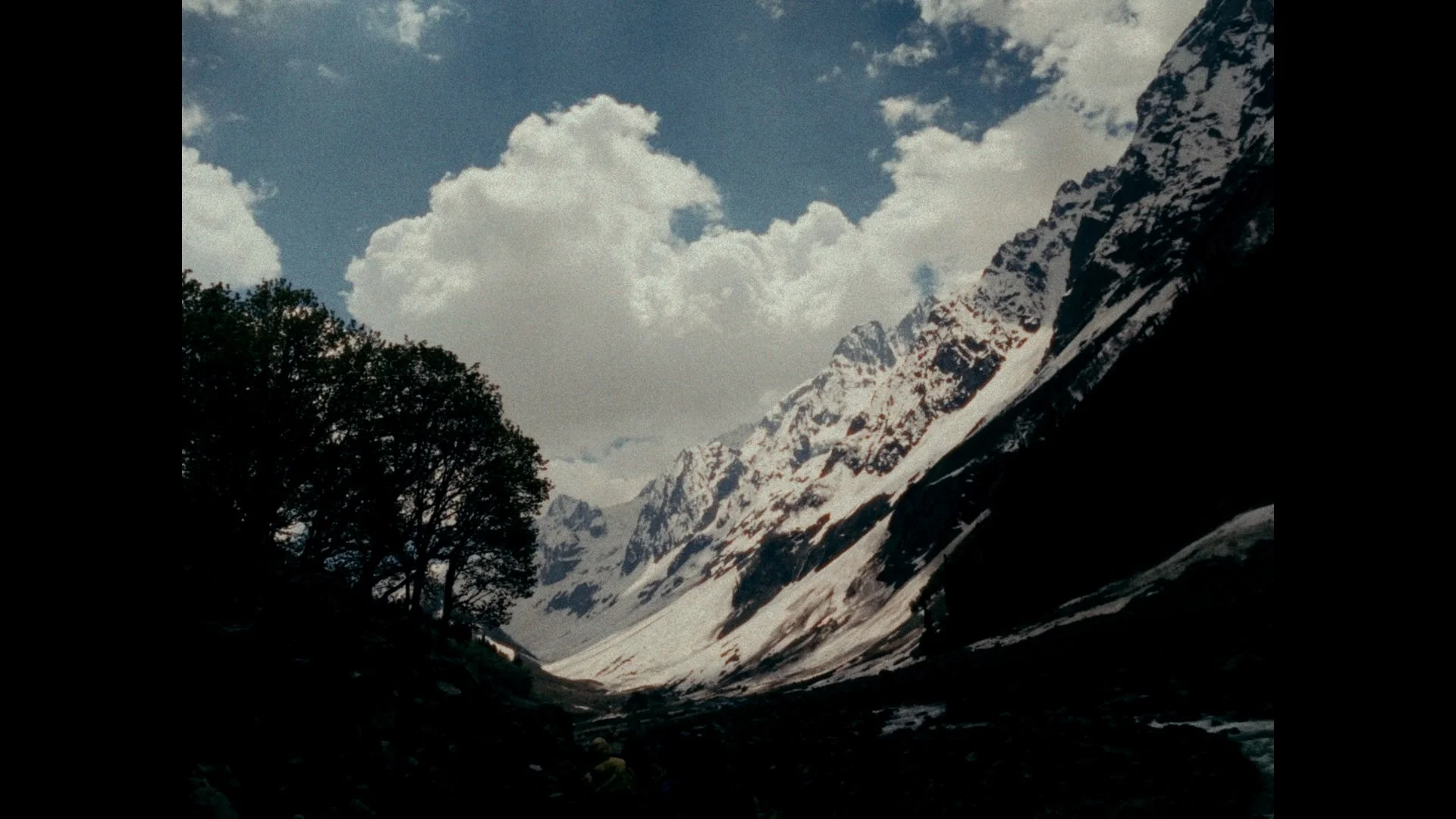 Snow-capped mountains under a partly cloudy sky, with a dark forest at the base of the mountains.