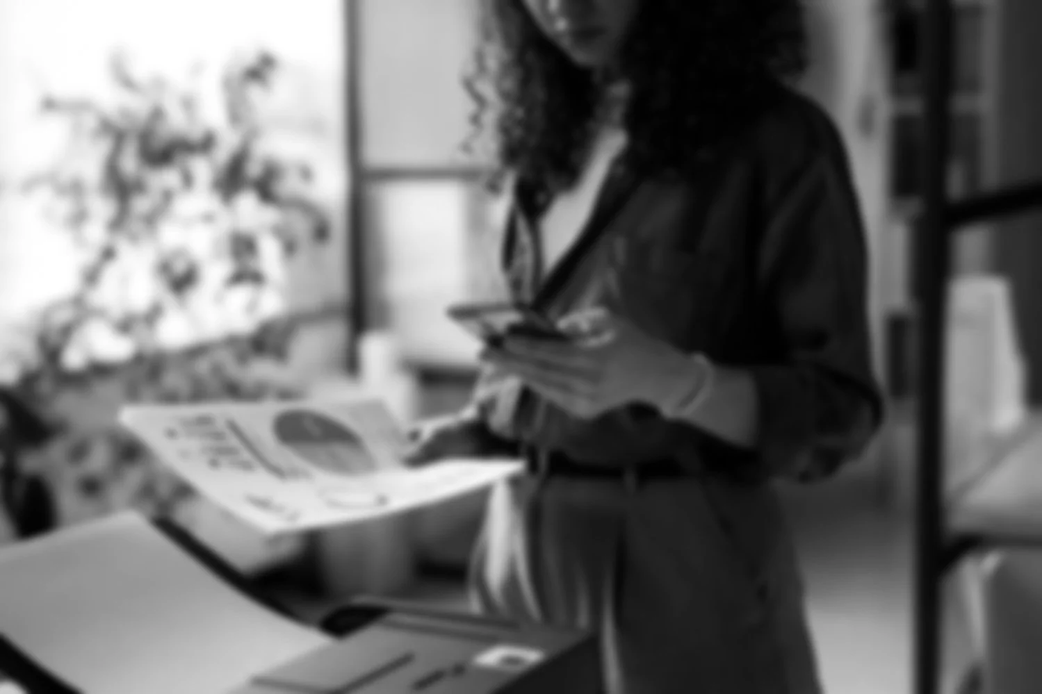 A person with curly hair wearing a dark shirt, shopping in a grocery store, examining items and looking at a phone.