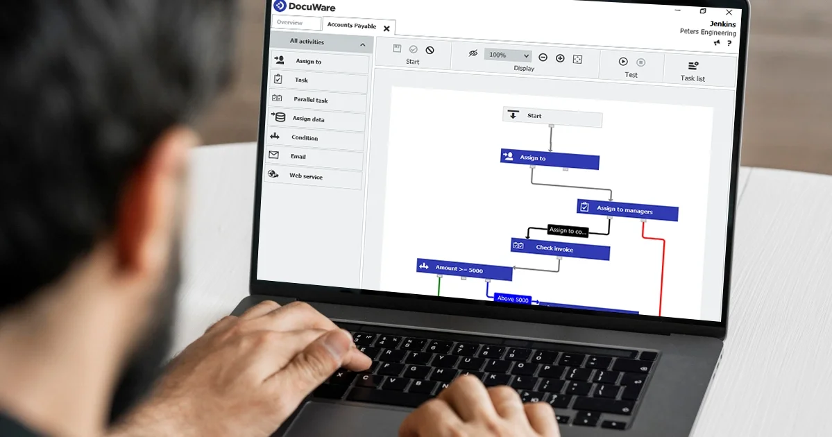 Person using a laptop to view a flowchart or process diagram in the DocuWare software, with various task steps like assigning, checking invoices, and categorizing amounts.