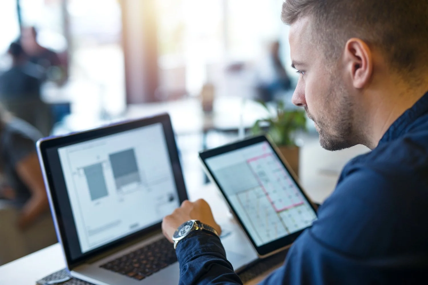 A man working at a desk with a laptop and tablet, analyzing graphs and maps.