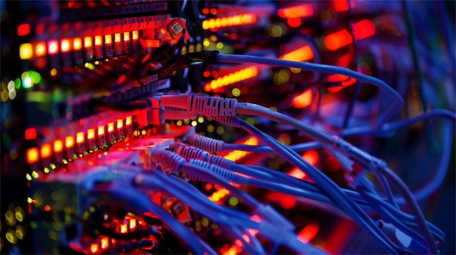 Close-up of a server rack with multiple network cables connected, illuminated by colorful LED lights in red, yellow, green, and blue.