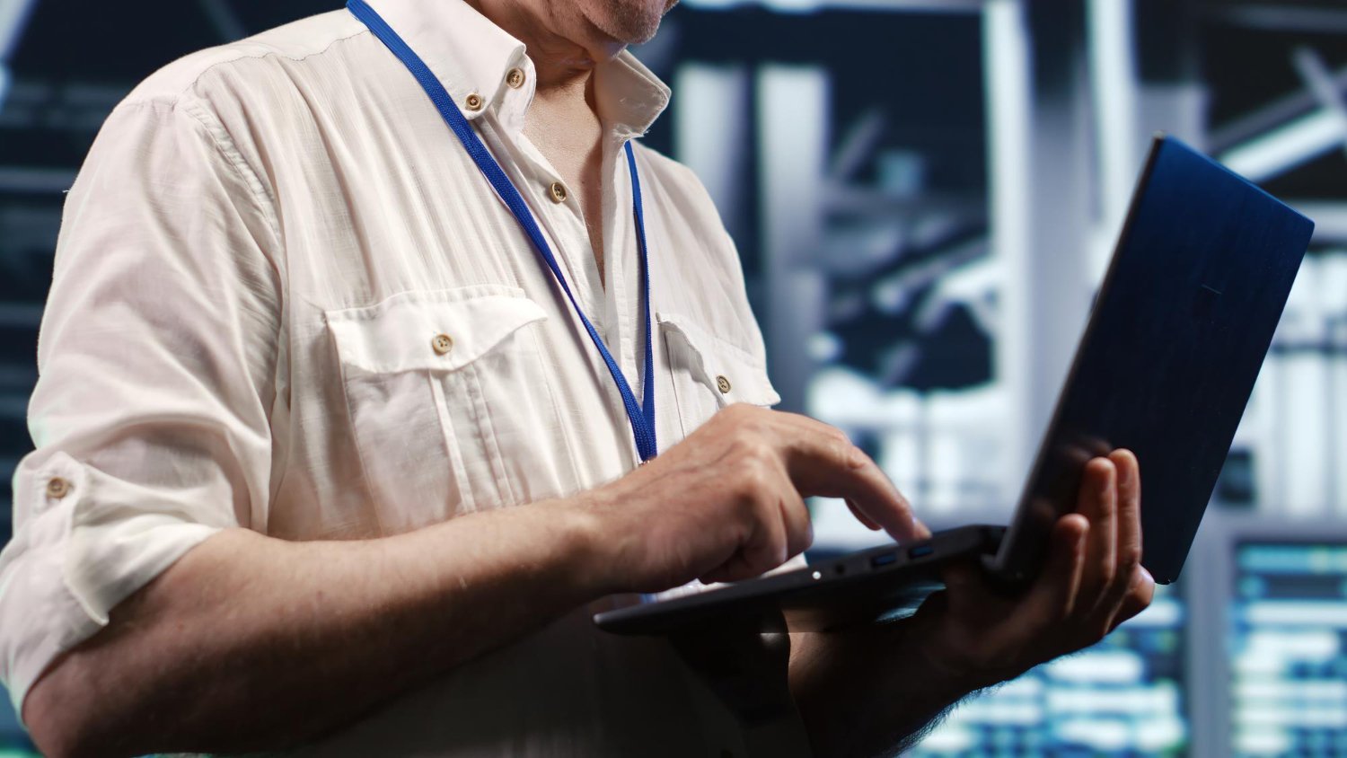 A person using a laptop in a data center with server racks in the background.