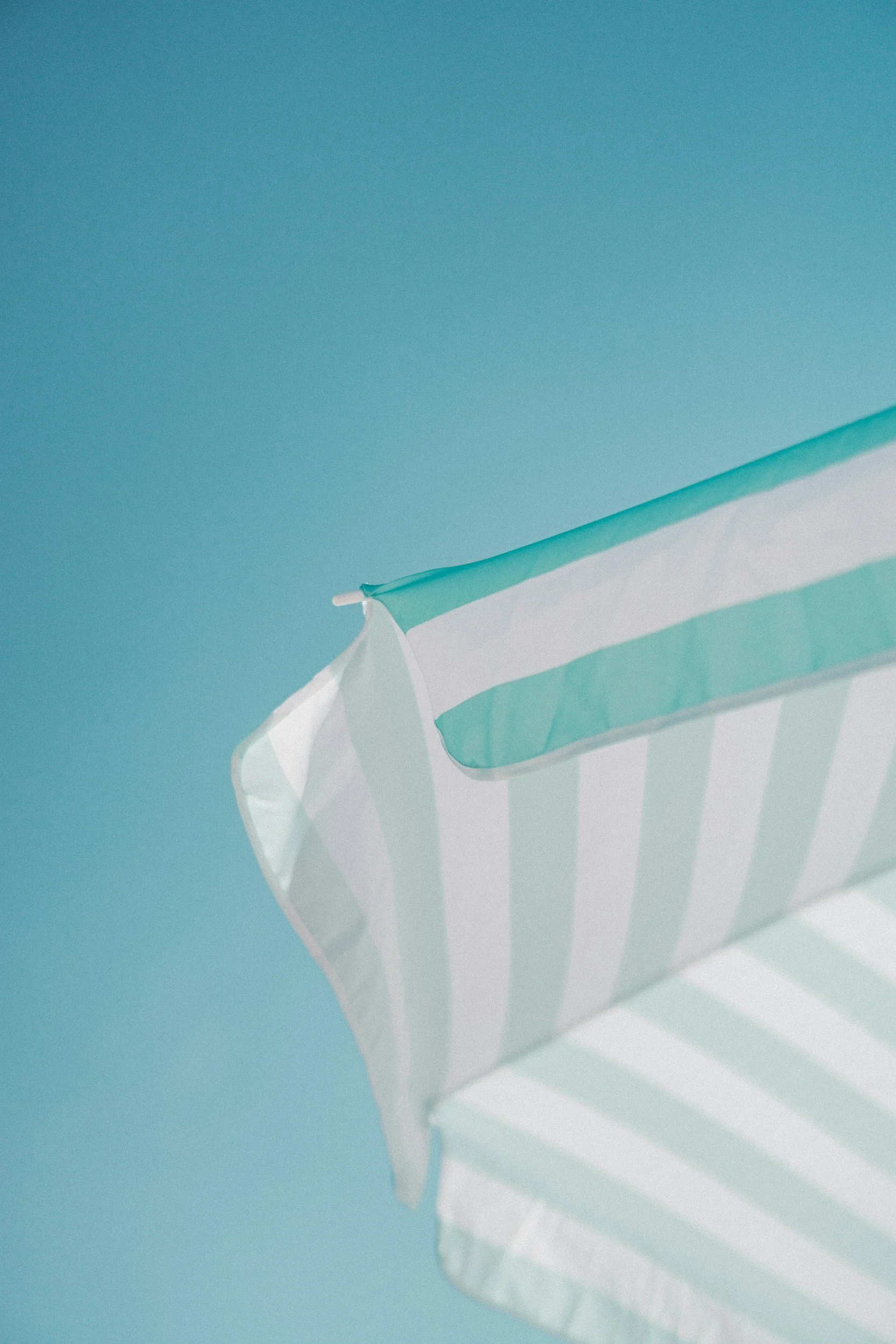 Vista en ángulo de una estructura de toldo o quiosco con rayas blancas y azul claro, con fondo azul y sin personas.