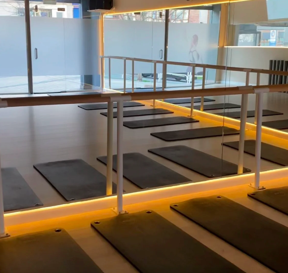 Yoga studio with black mats arranged on light-colored floor, mirrored wall, and large glass windows showing a street view outside.