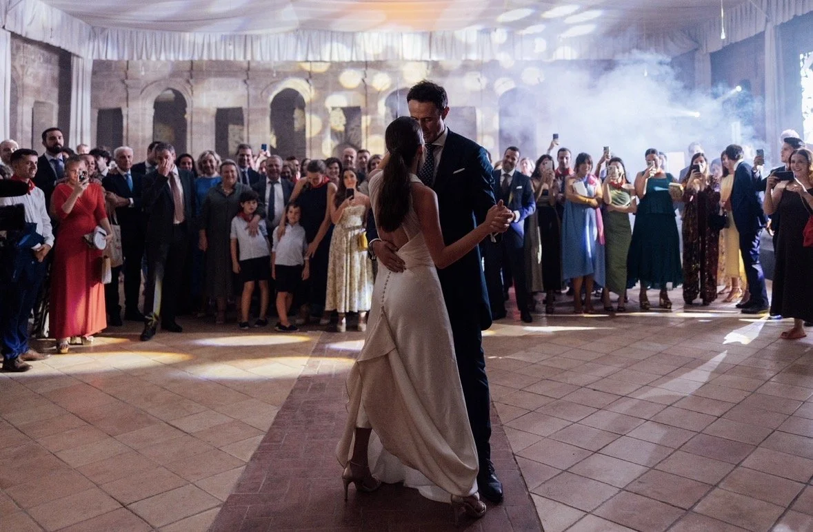 Pareja bailando en la pista de una boda, rodeada de invitados y decoraciones elegantes.