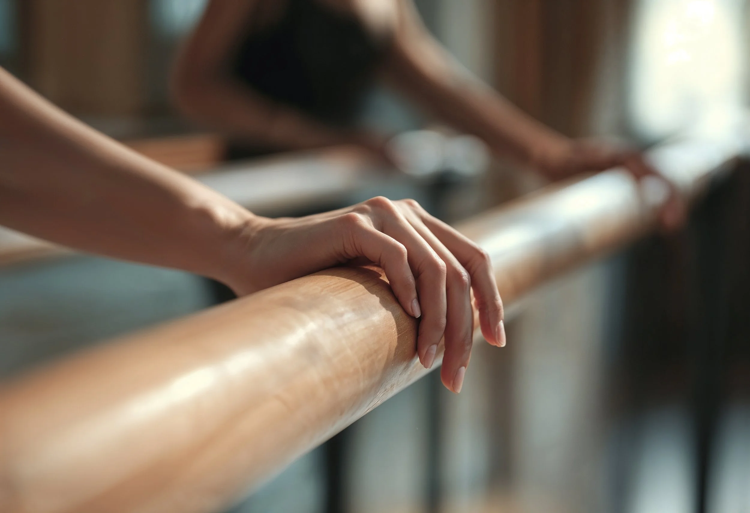 Close-up of a person's hand resting on a wooden ballet barre during a dance class.