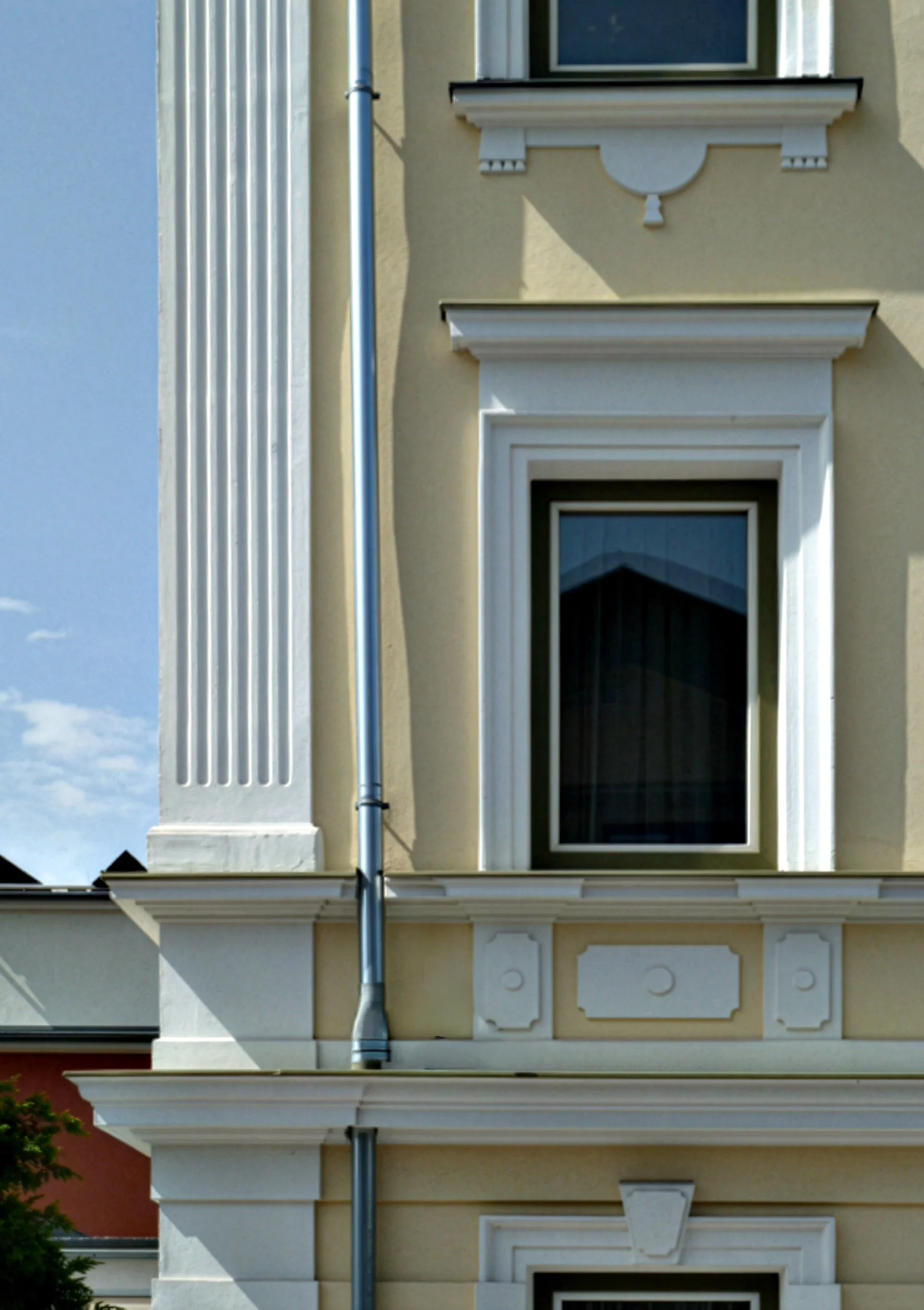 Ein Fassadenabschnitt eines klassischen Gebäudes mit weißen dekorativen Elementen und einem großen Fenster