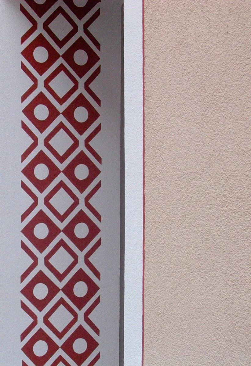 Nahaufnahme einer Wand mit einem dekorativen Muster in Rot und Weiß sowie eine Textur in hellbeige.