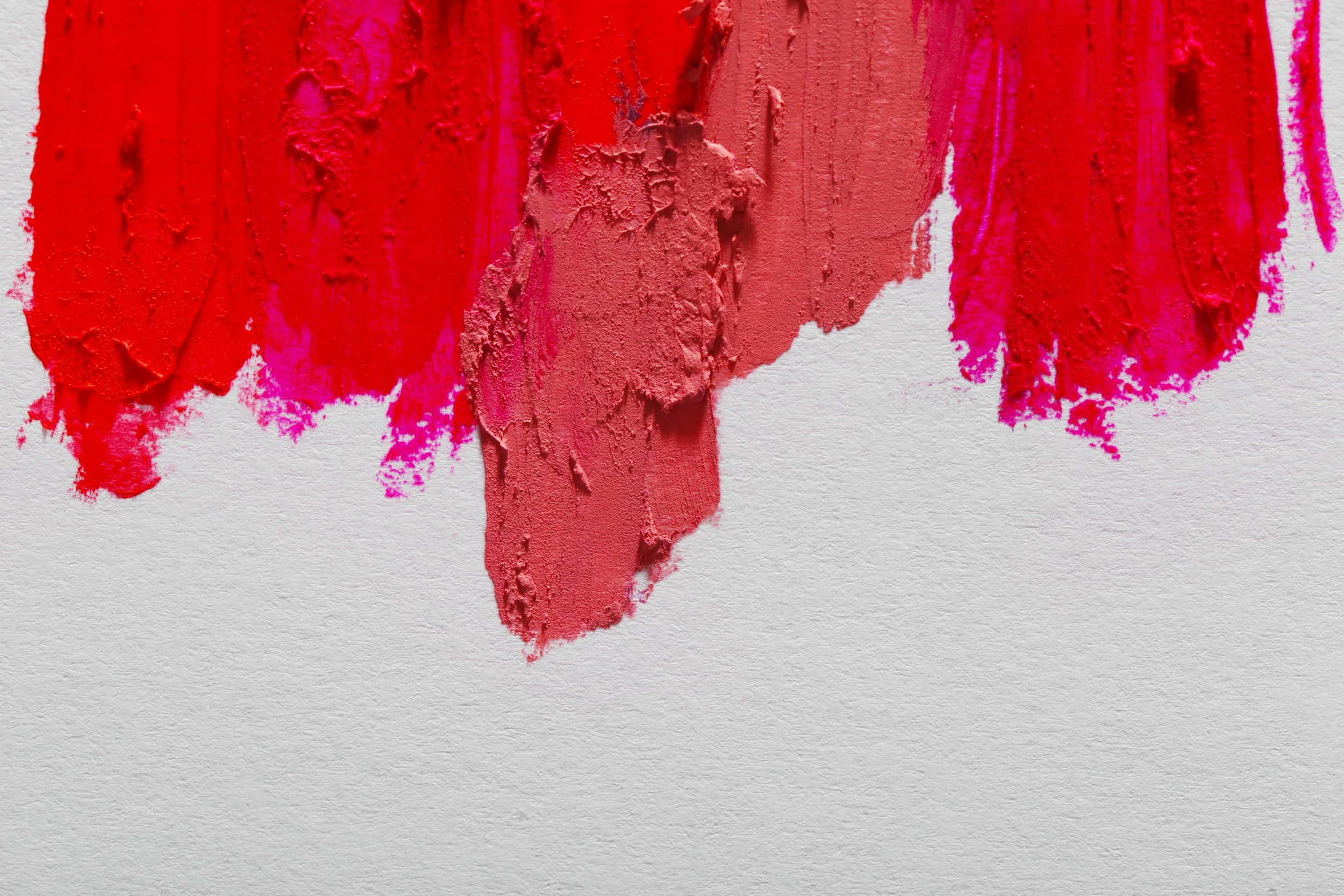 Nahaufnahme von Lippenstift-Farben in Rot- und Pink-Tönen auf einer weißen Textur