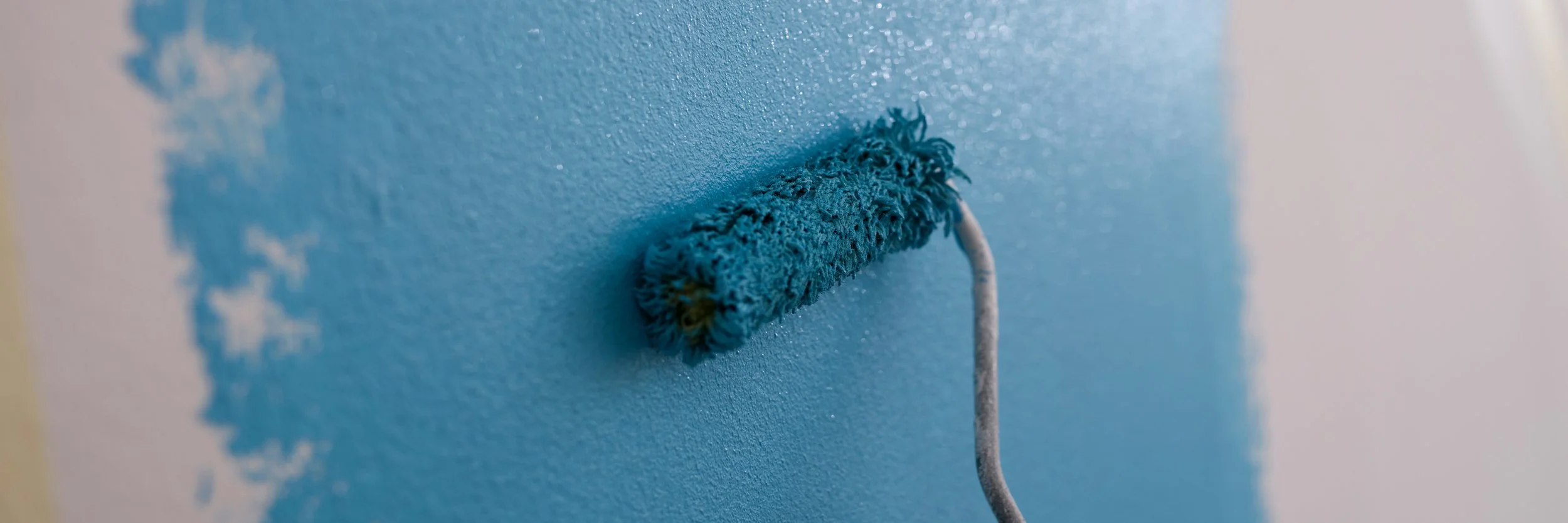 Nahaufnahme eines blauen Farbrollers, der an einer Wand mit hellblauer Farbe gestrichen wird.