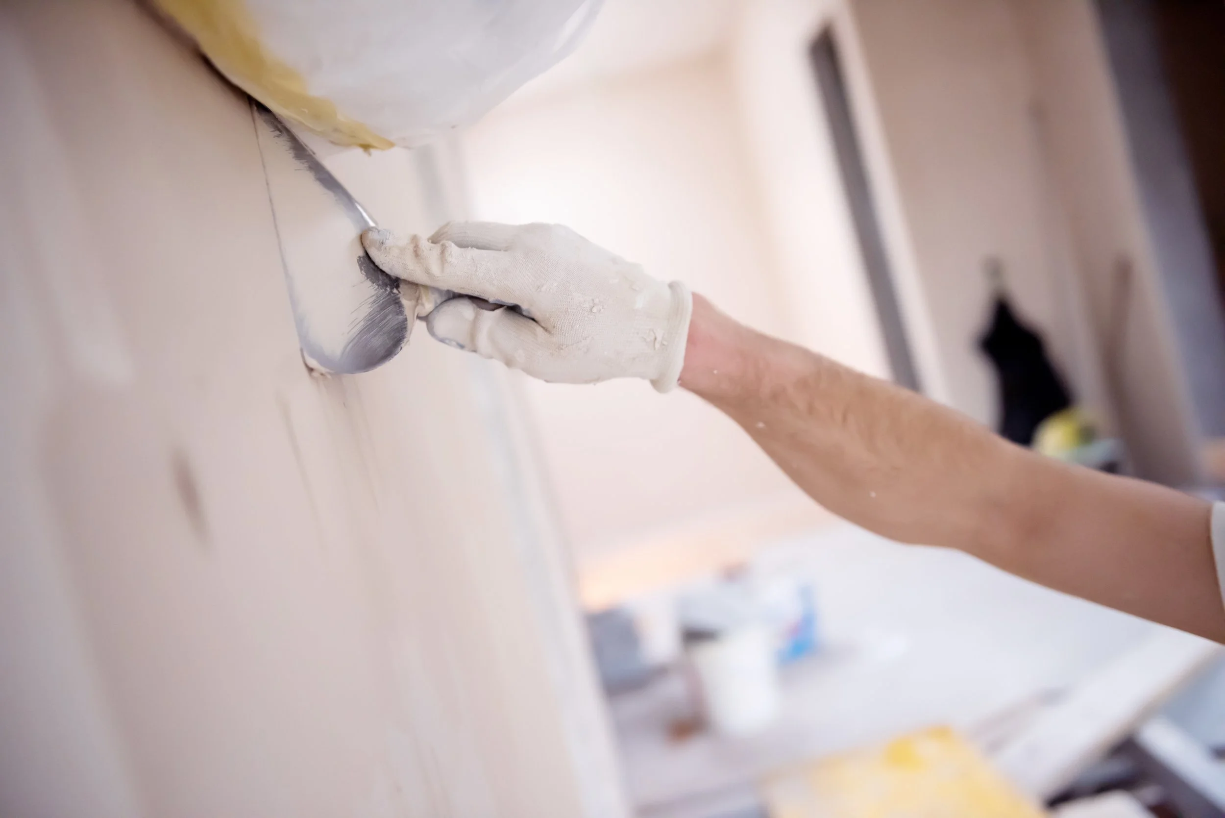 Hand in einem weißen Handschuh, der eine Wand mit einem Spachtel bearbeitet
