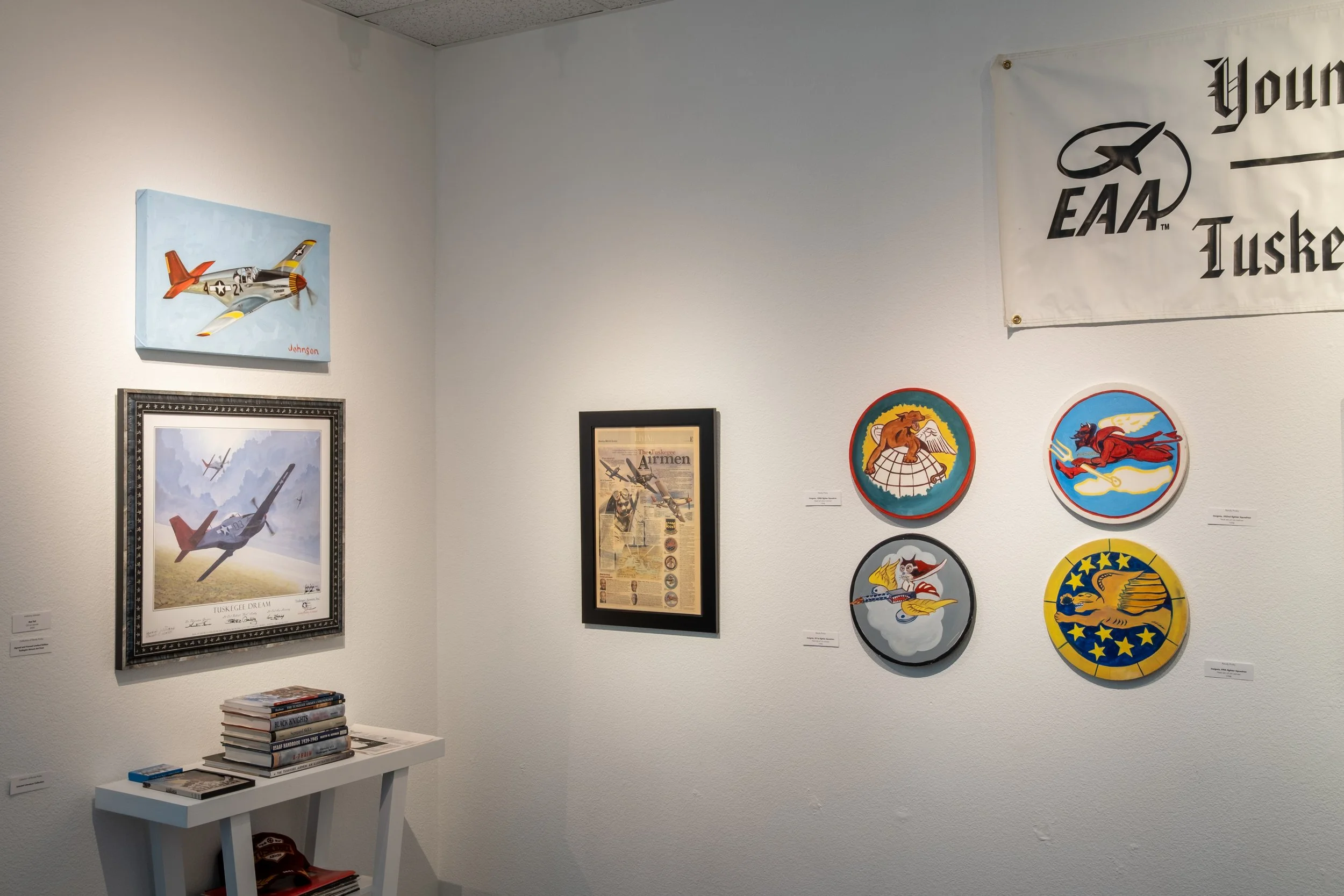 "Red Tail" by Anthony Johnson, 2024 ; "Tuskegee Airmen Signed Print, Literature Collection and NEwspaper Clipping" Courtesy the Collection of Randy Proby ; "Tuskegee Airmen Fighter Squadron Insignia Paintings" by Randy Proby