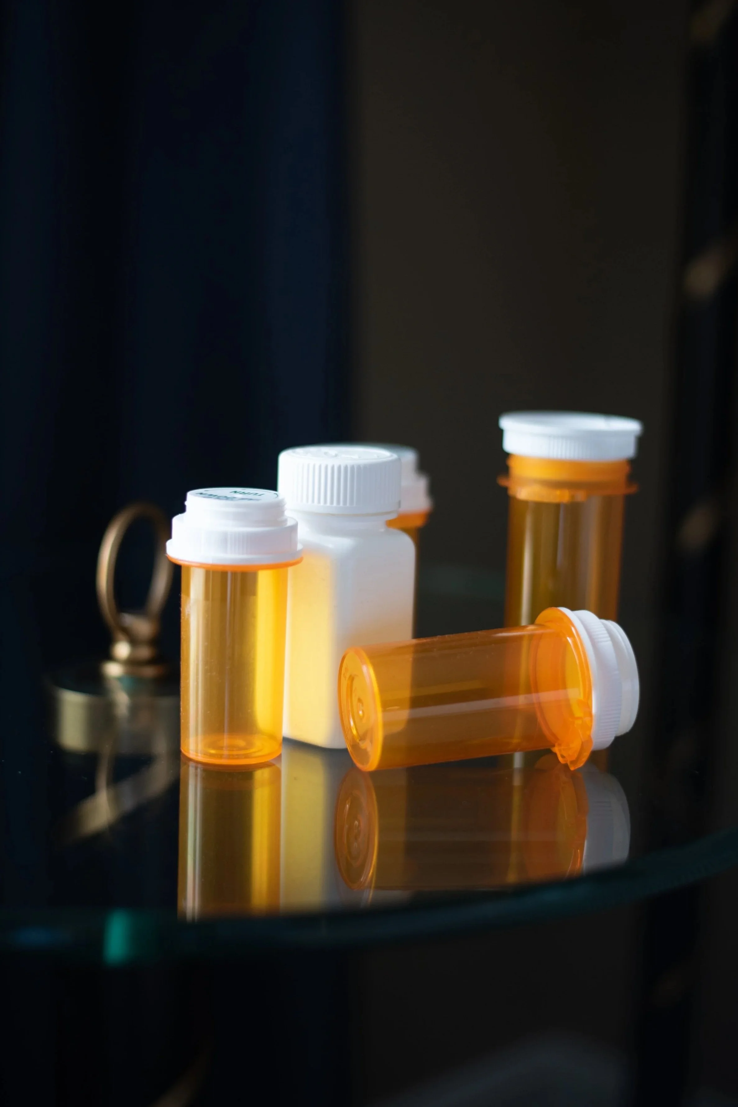 Several orange pill bottles and white prescription bottles on a reflective surface with dark background.