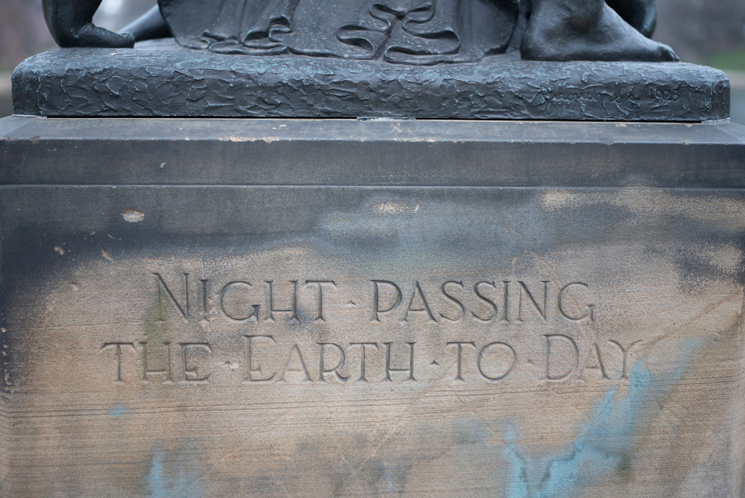 Close-up of a bronze monument base engraved with the words 'Night Passing the Earth to'.