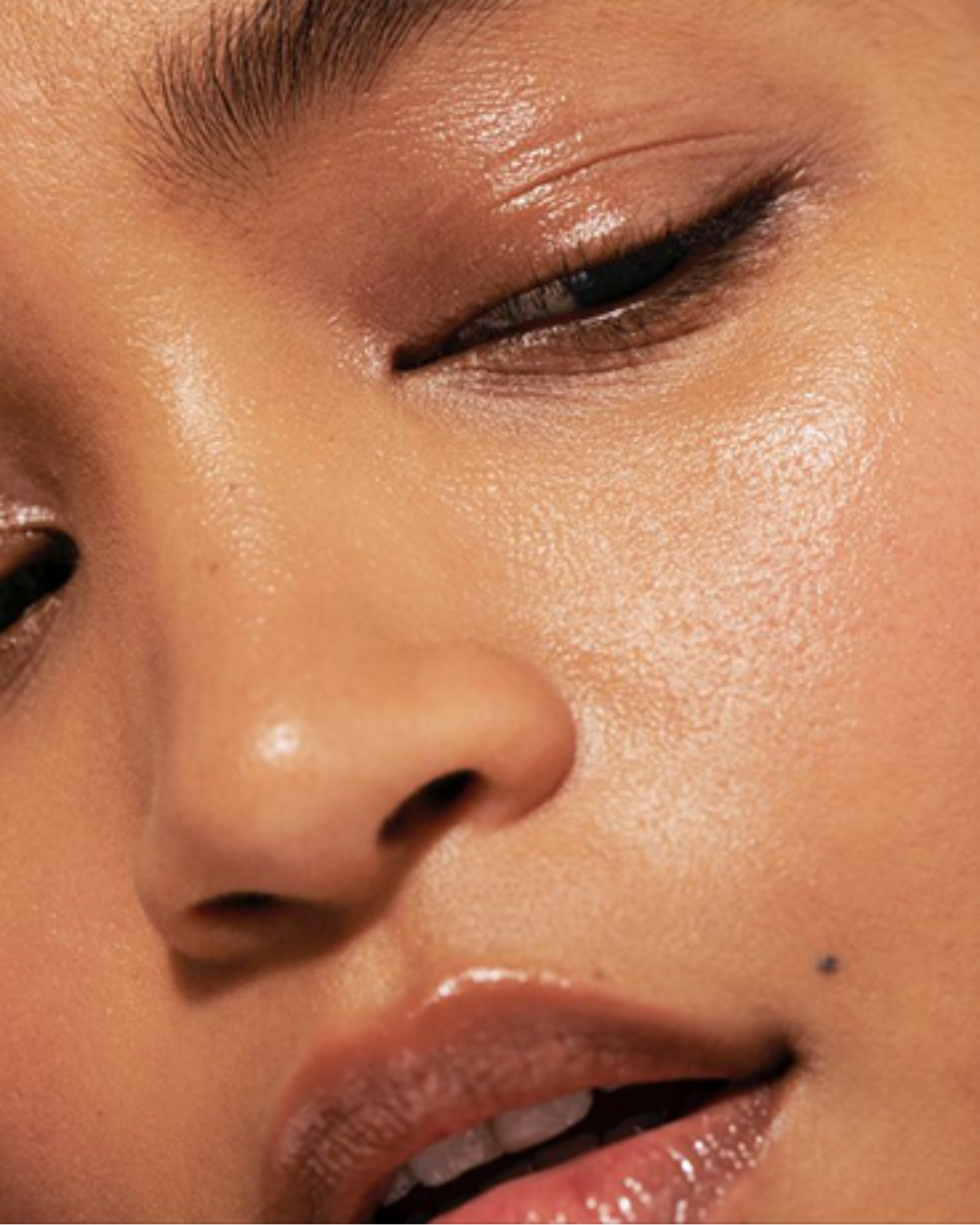 Close-up of a person's face showing one closed eye, nose, and partially opened lips with makeup.