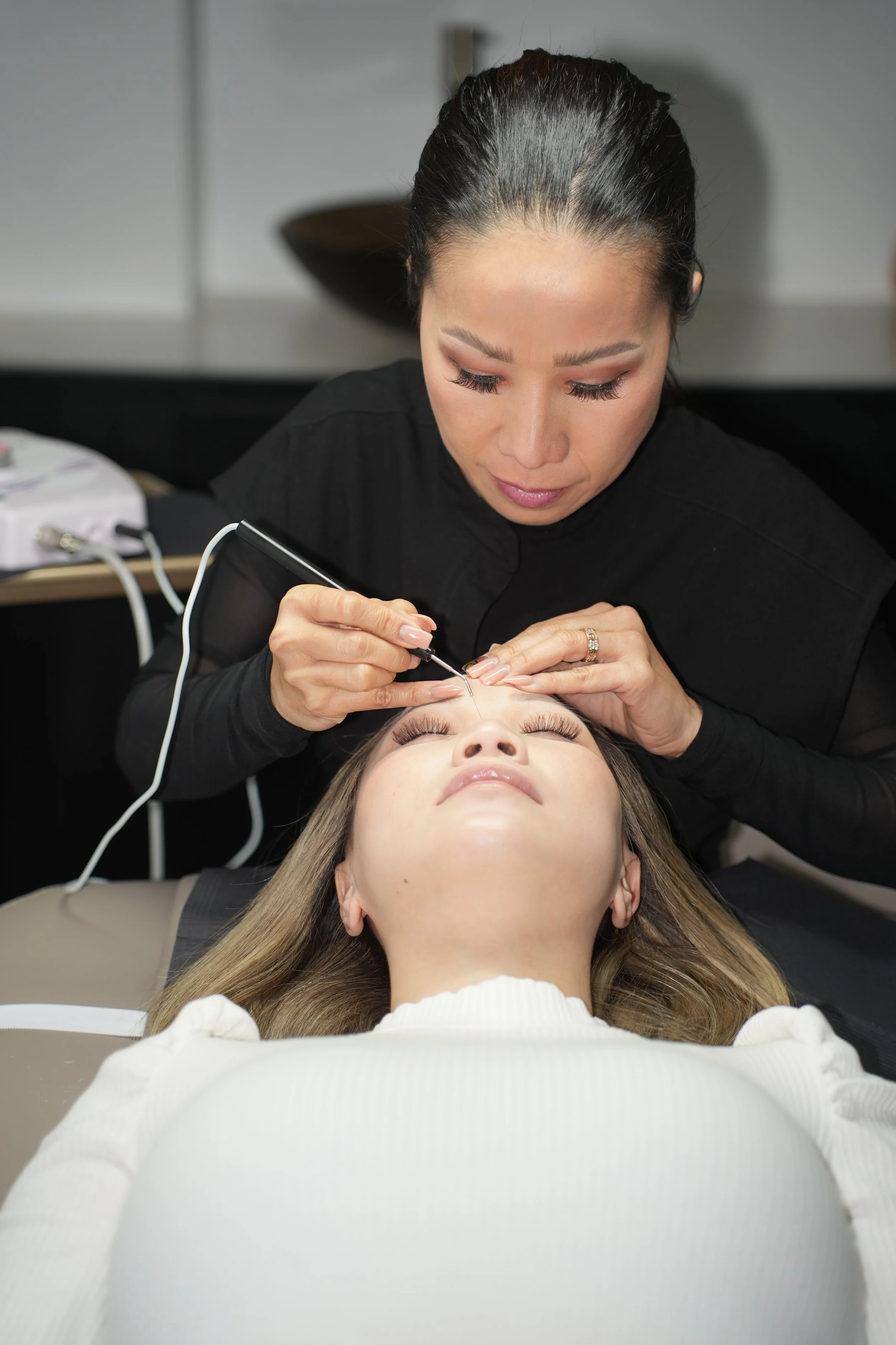 A woman receiving a facial treatment from an esthetician in a spa or clinic setting.